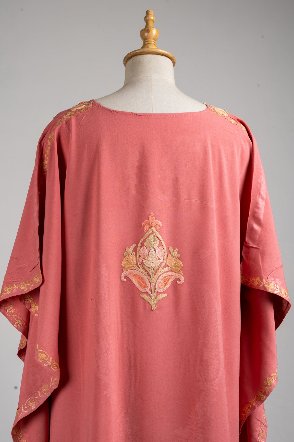 Close-up of the blush-rose kaftan’s back, with a pointed champagne-and-peach floral motif between the shoulders