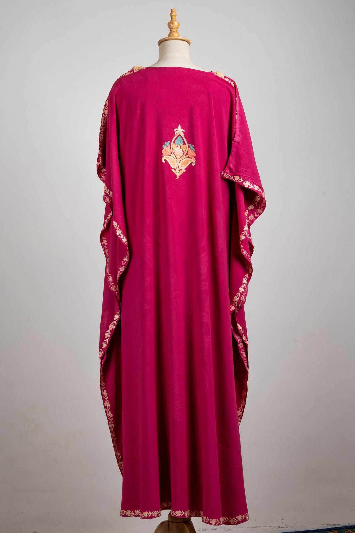 Full back view of the fuchsia kaftan, with one floral motif and narrow embroidery along the loose sleeves and hem