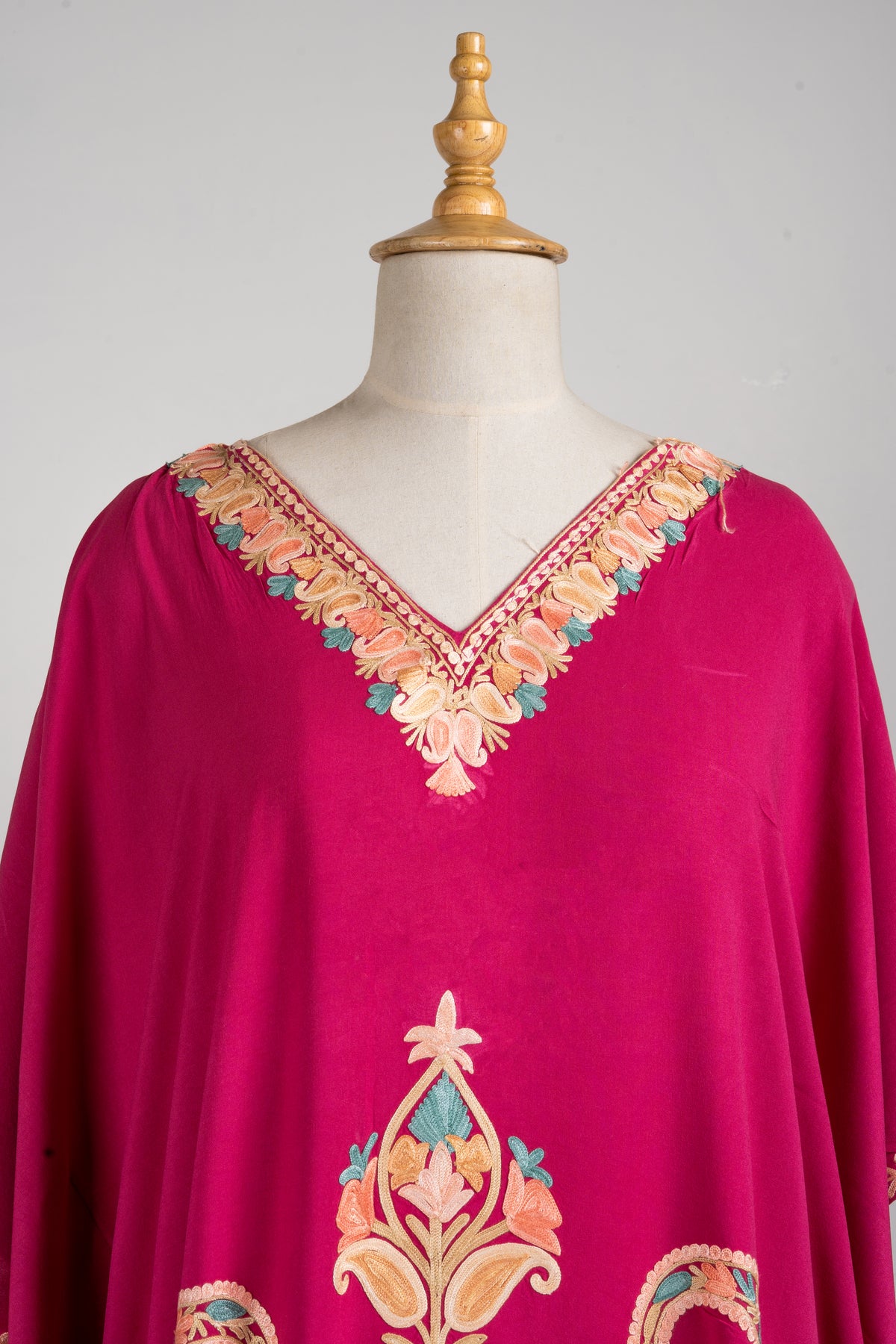 Close view of the fuchsia kaftan’s V-neck, edged with peach and beige flowers, and a small floral motif below