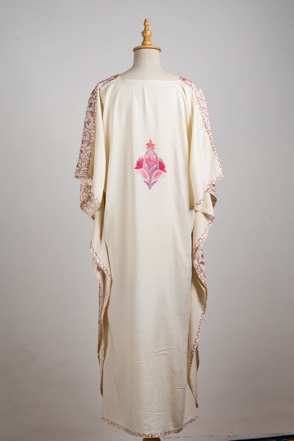 Back of a cream kaftan with a mostly plain centre, one pink Aari floral motif and embroidered draped sleeve edges