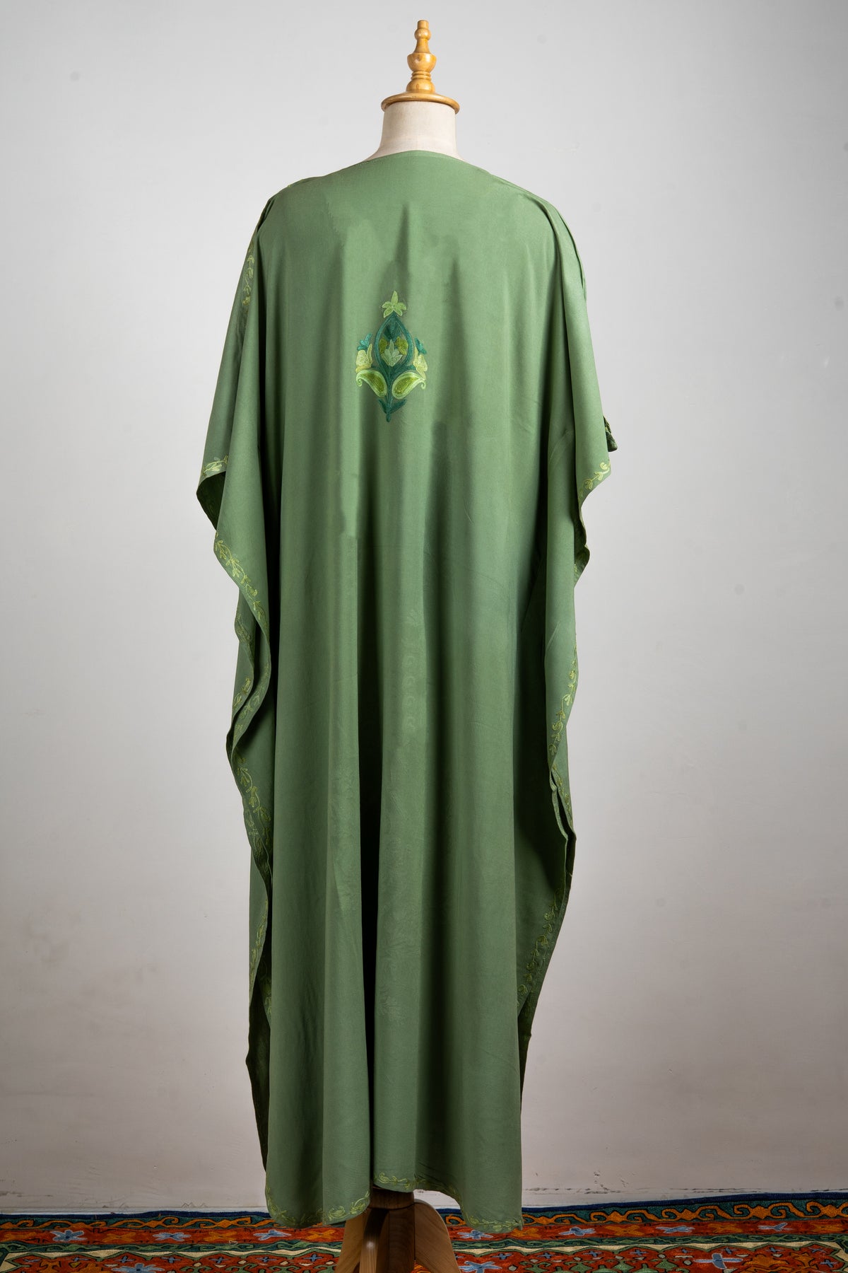 Full back view of the olive-green kaftan with a small embroidered motif, flowing sleeves and a long plain body.