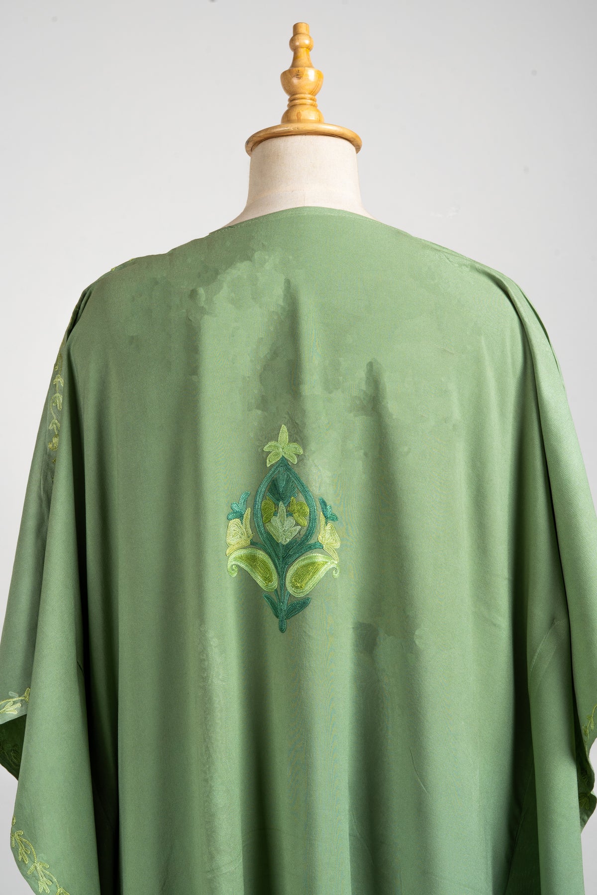 Upper back of the olive kaftan with a single green and yellow floral motif beneath the plain round neckline.