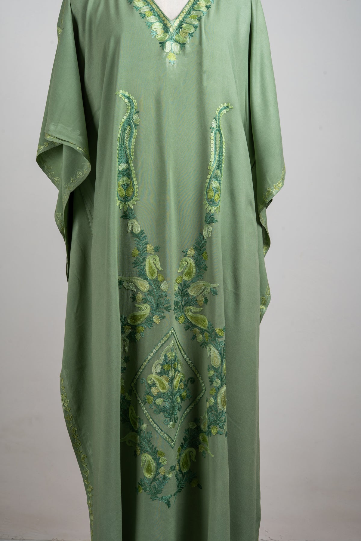 Detail of the kaftan front embroidery with long paired paisleys, leafy branches and a central diamond motif in green and yellow.