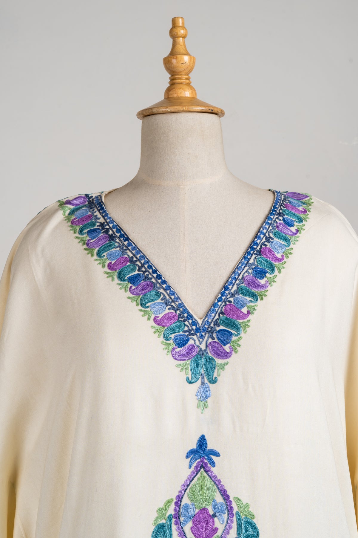 Close-up of the cream kaftan’s V-neck, with blue, teal and lavender embroidered leaves and green accents