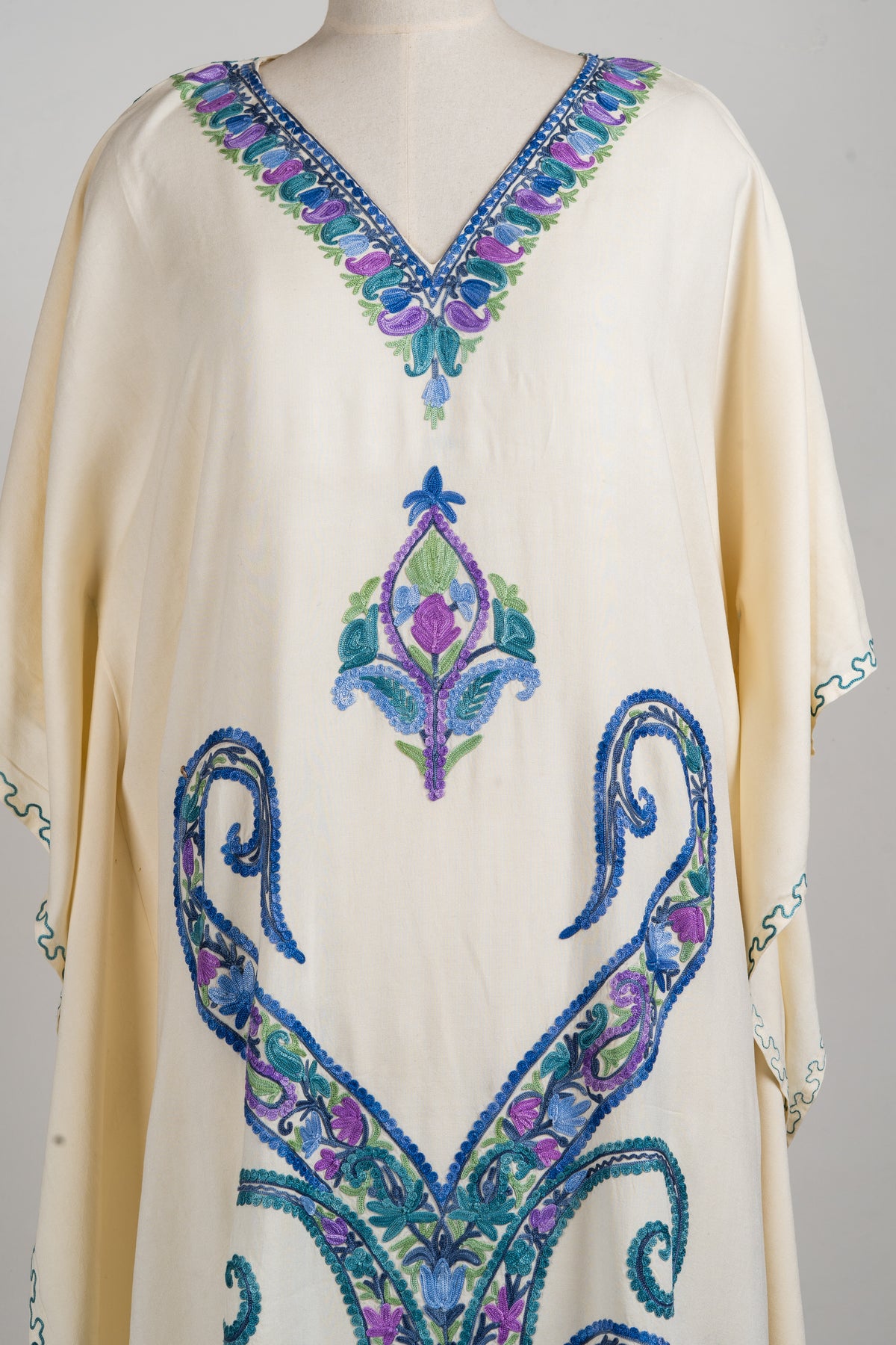 Detail of the cream kaftan’s front, with a pointed floral medallion above large symmetrical teal-and-blue scrolls