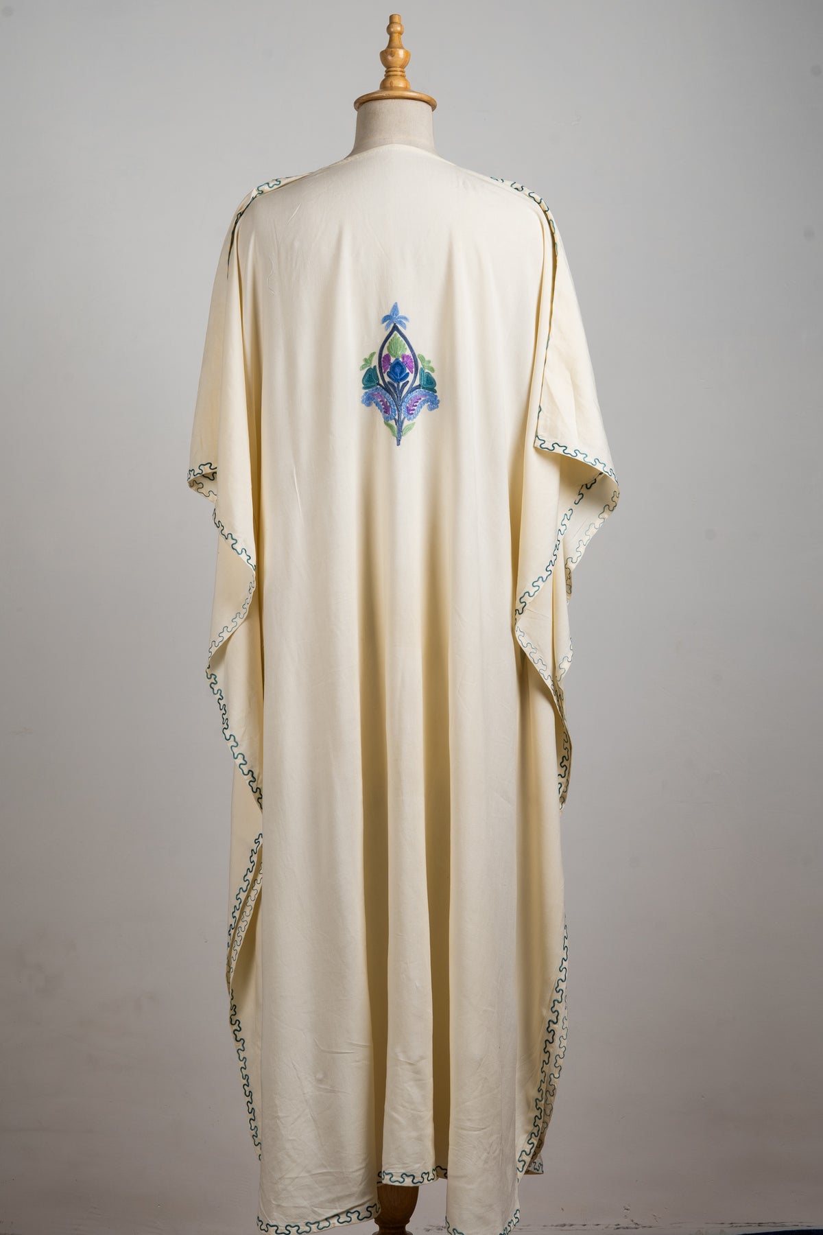Back of the cream kaftan, showing loose draped sleeves, narrow wavy edging and a small coloured motif