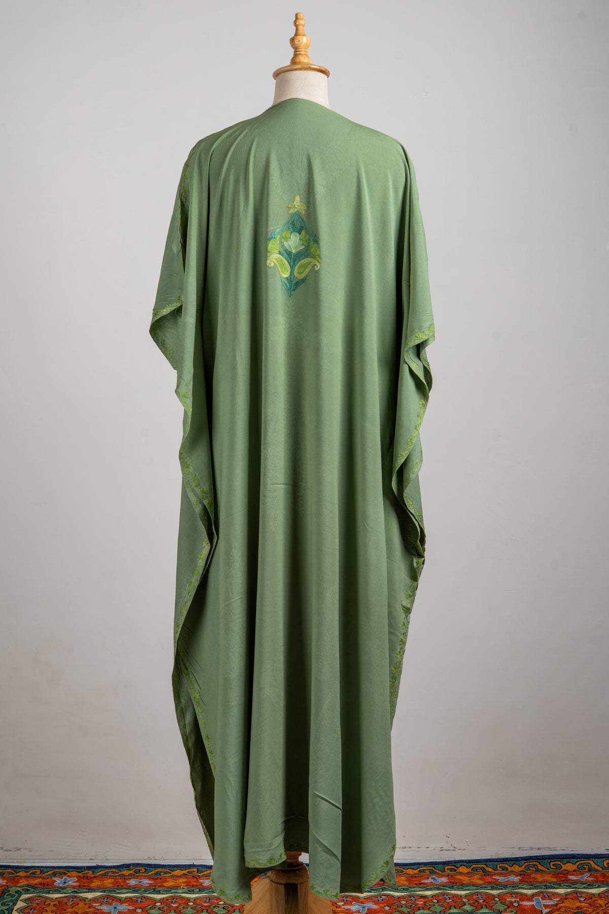 Back of a flowing olive-green kaftan with one small Aari motif high in the centre and narrow embroidered sleeve edges