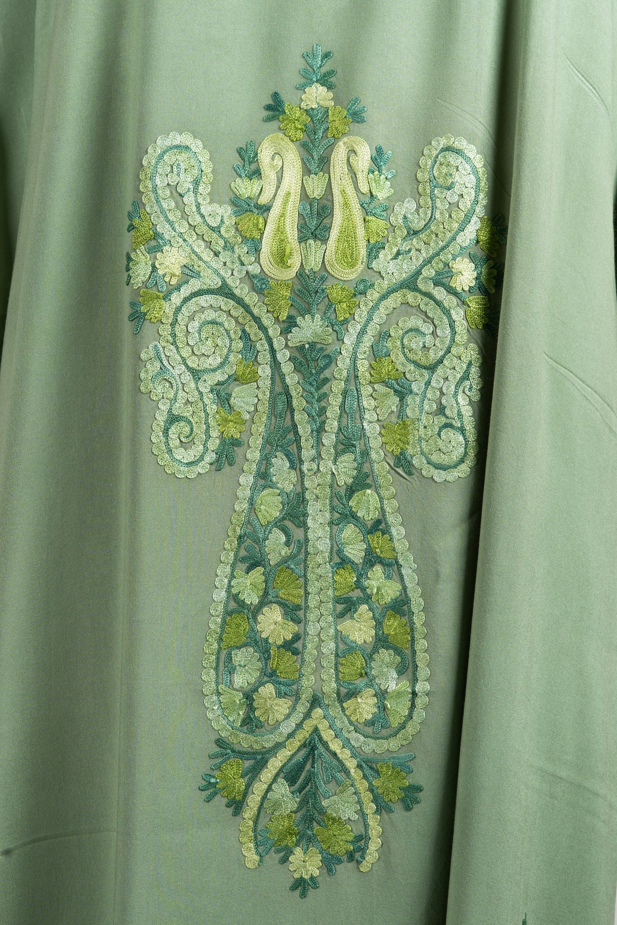 Close-up of a long symmetrical Aari paisley crest in pale green, teal and lemon on olive-green fabric