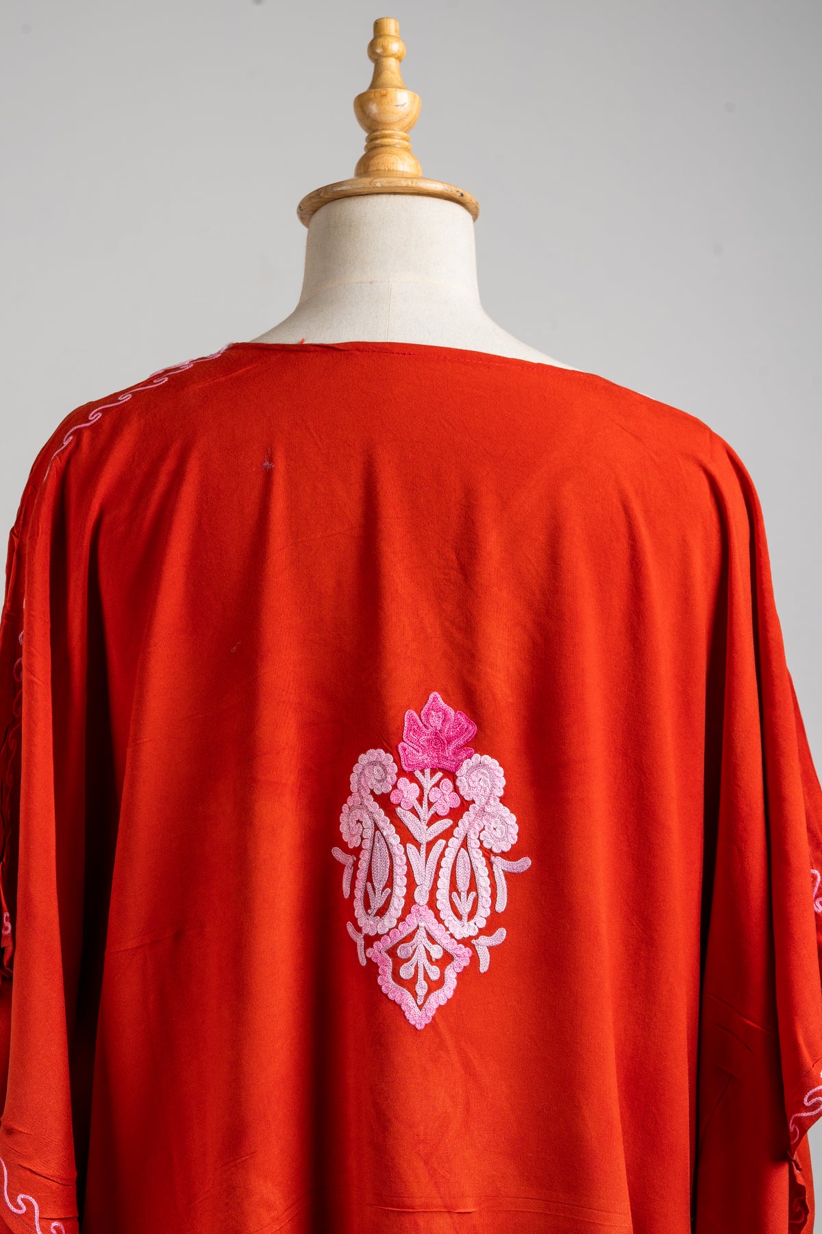 Upper back detail of the crimson kaftan showing a small pink floral and paisley motif beneath the plain round neckline.