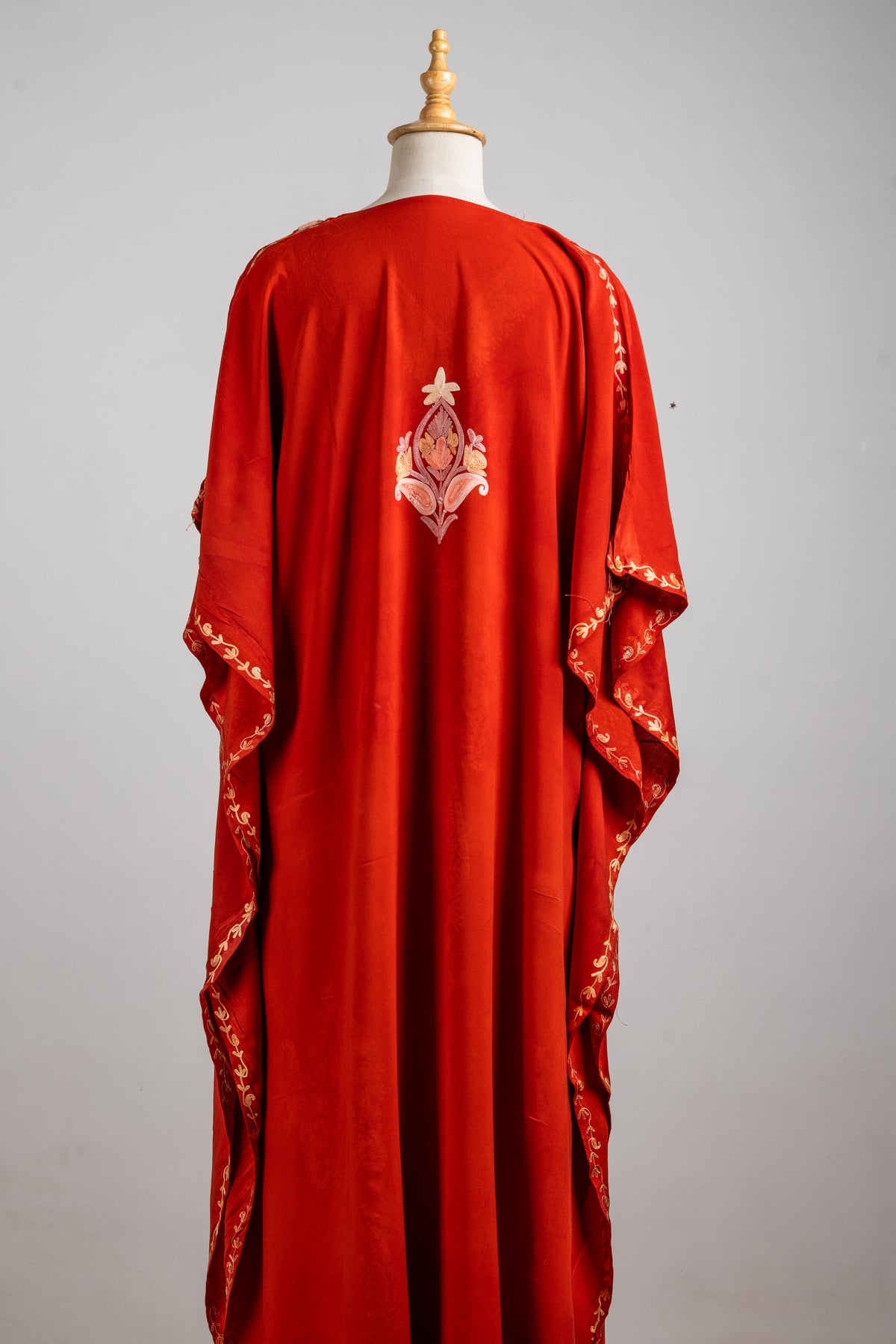 Full back view of the rust-red kaftan, showing a single pale floral motif and embroidered sleeve edges