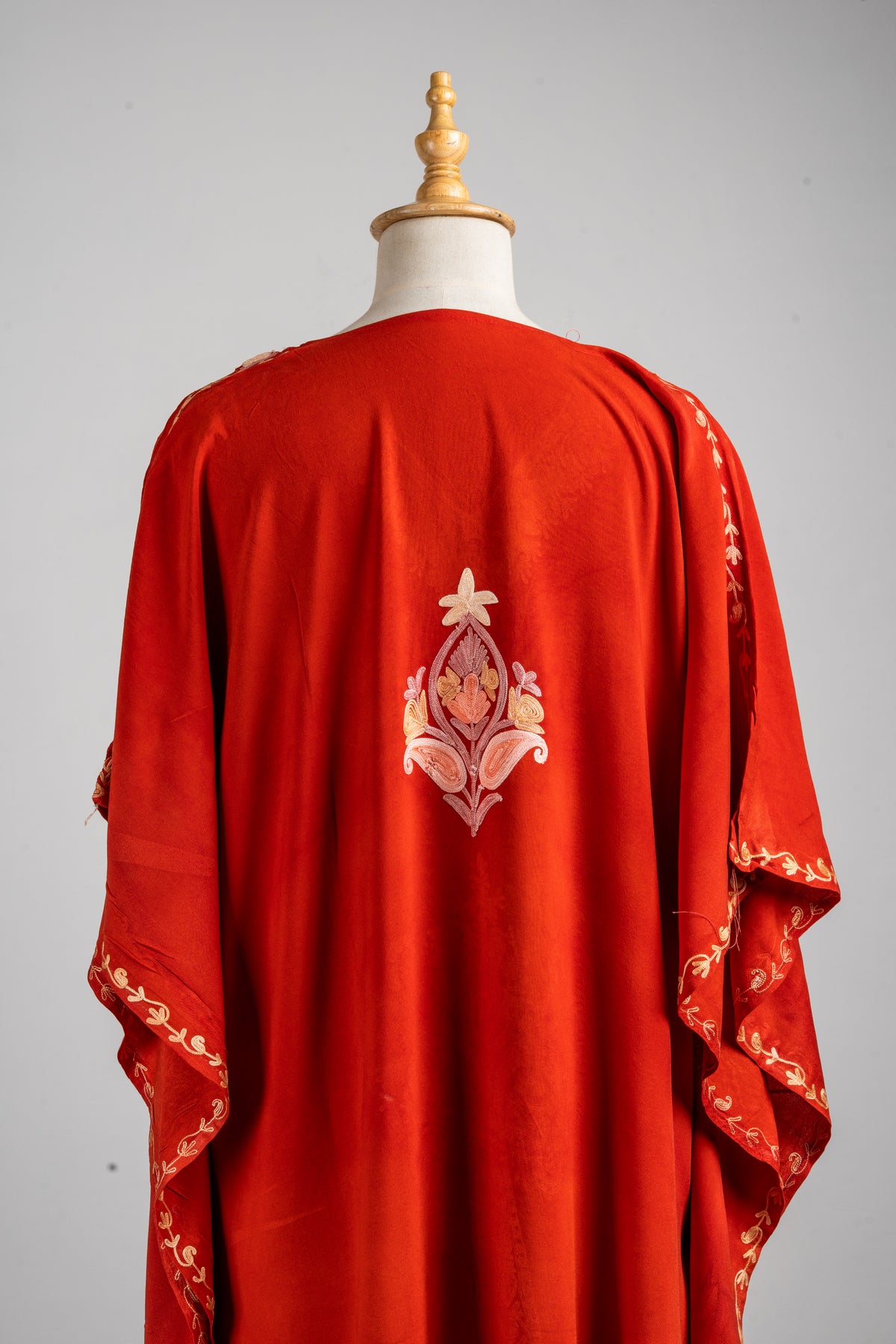 Close view of the rust-red kaftan’s back, with a peach and cream floral motif between draped sleeves