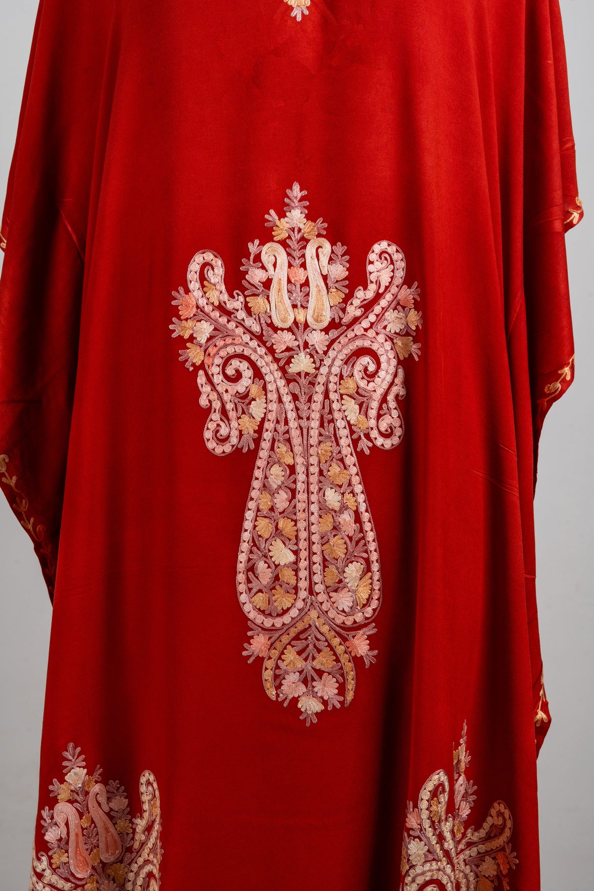 Detail of a large symmetrical peach and cream Aari medallion on the rust-red kaftan, filled with flowers and curling forms