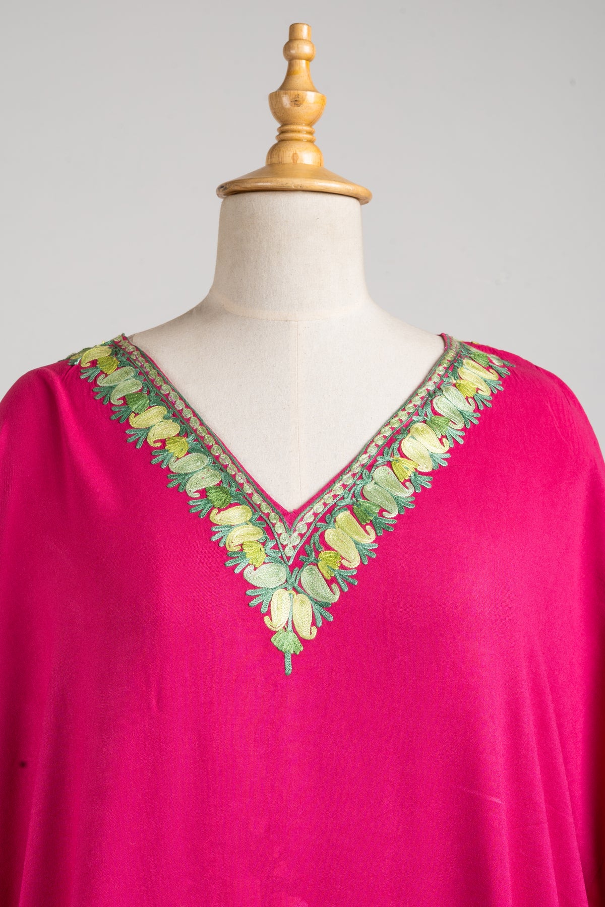 Close-up of the fuchsia kaftan’s V-neck with pale gold and green embroidered leaves and narrow patterned edging