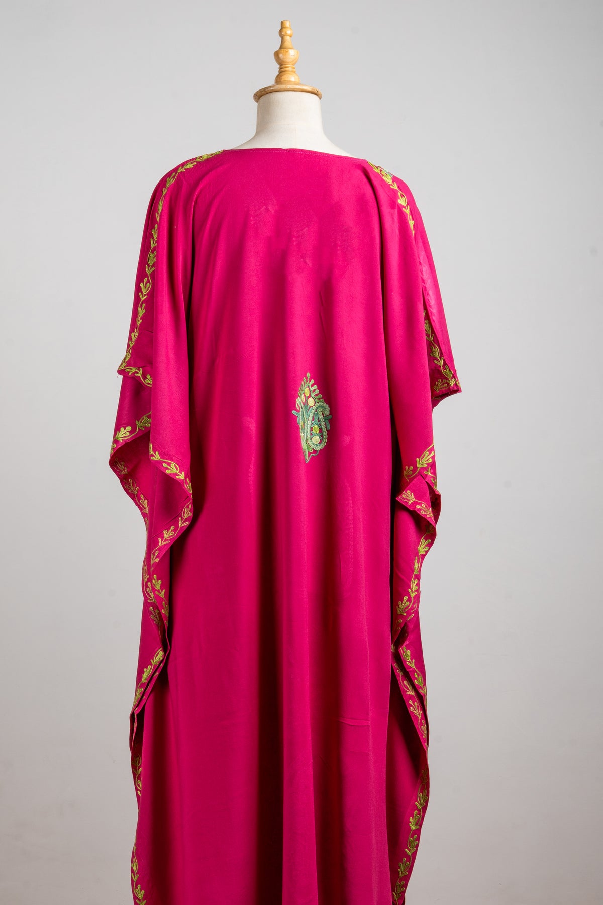 Back of a fuchsia kaftan, with a small green-and-gold motif and embroidered edges along the draped sleeves