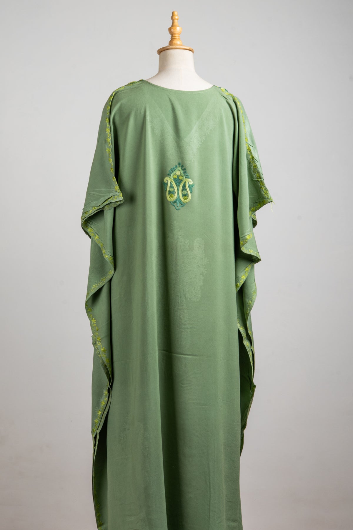 Back of a flowing green kaftan with a small lime and dark green Aari paisley motif high in the centre