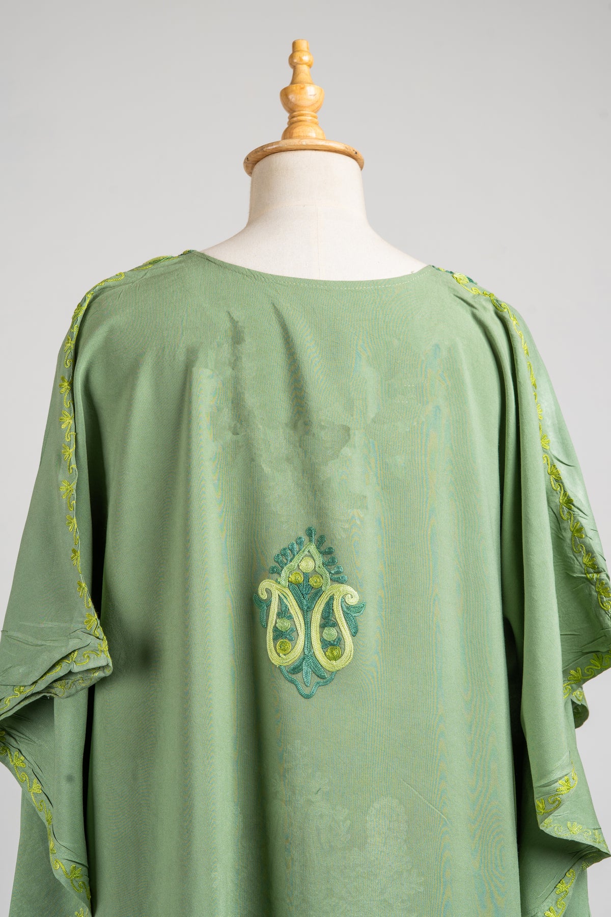 Upper back of a pastel-green kaftan with paired lime Aari paisleys and green leaves, between embroidered draped sleeve edges
