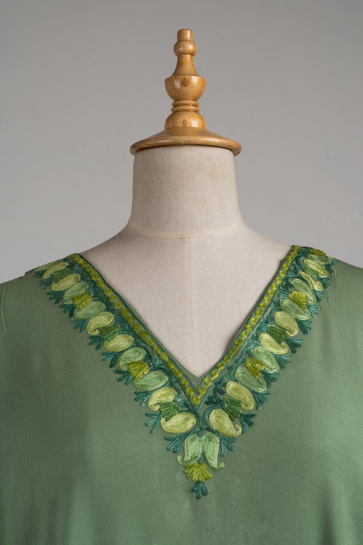 Detail of a green kaftan's V-neck bordered with pale lime Aari petals, dark green leaves and narrow patterned lines