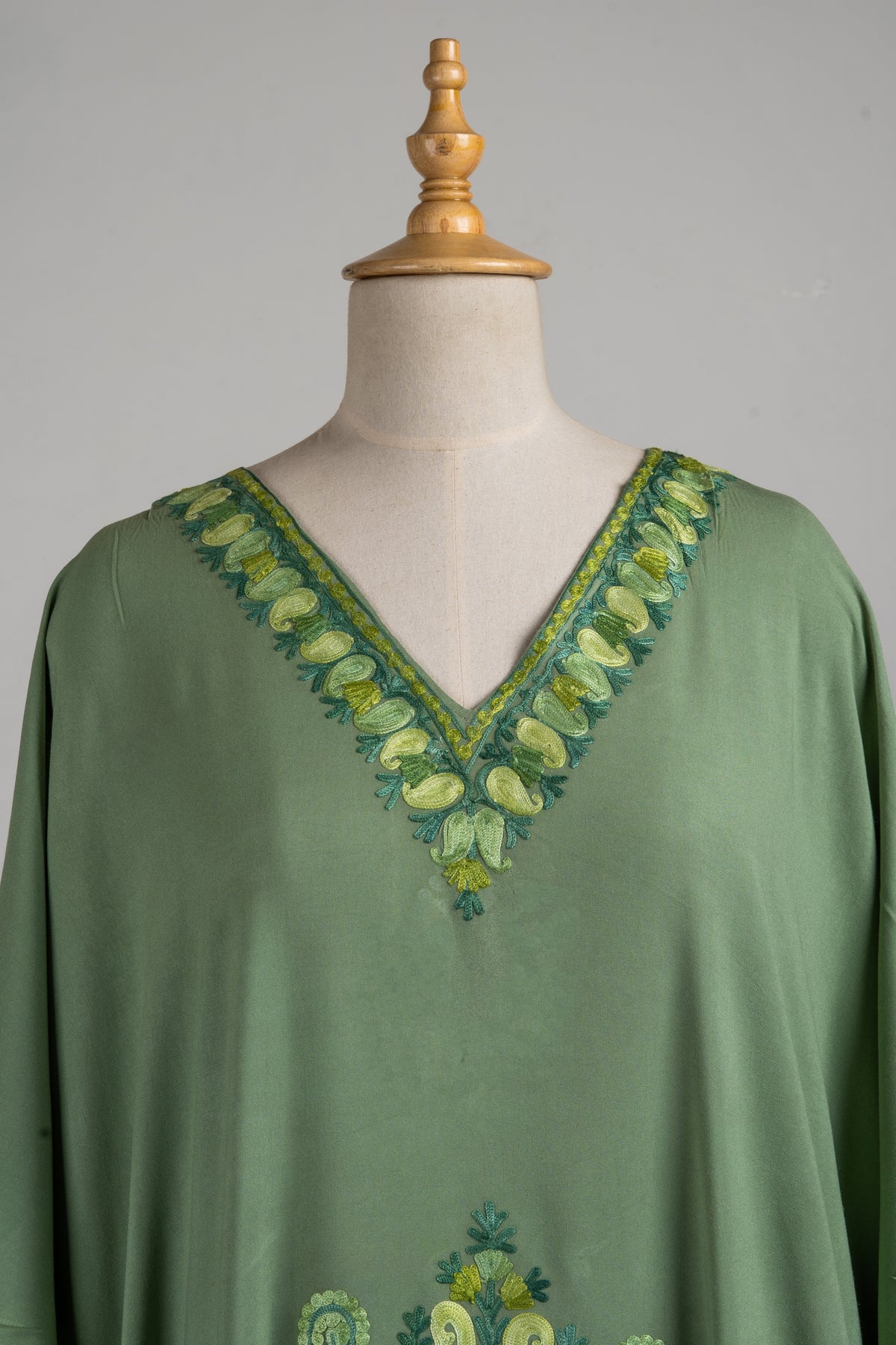 Upper front of a green kaftan with pale lime Aari petals and darker green leaves around the V-neck