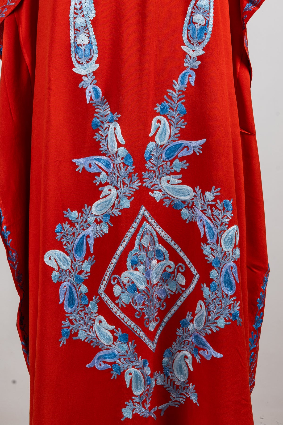 Close-up of the red kaftan front with pale blue paisleys and leafy vines surrounding a diamond-shaped floral panel.