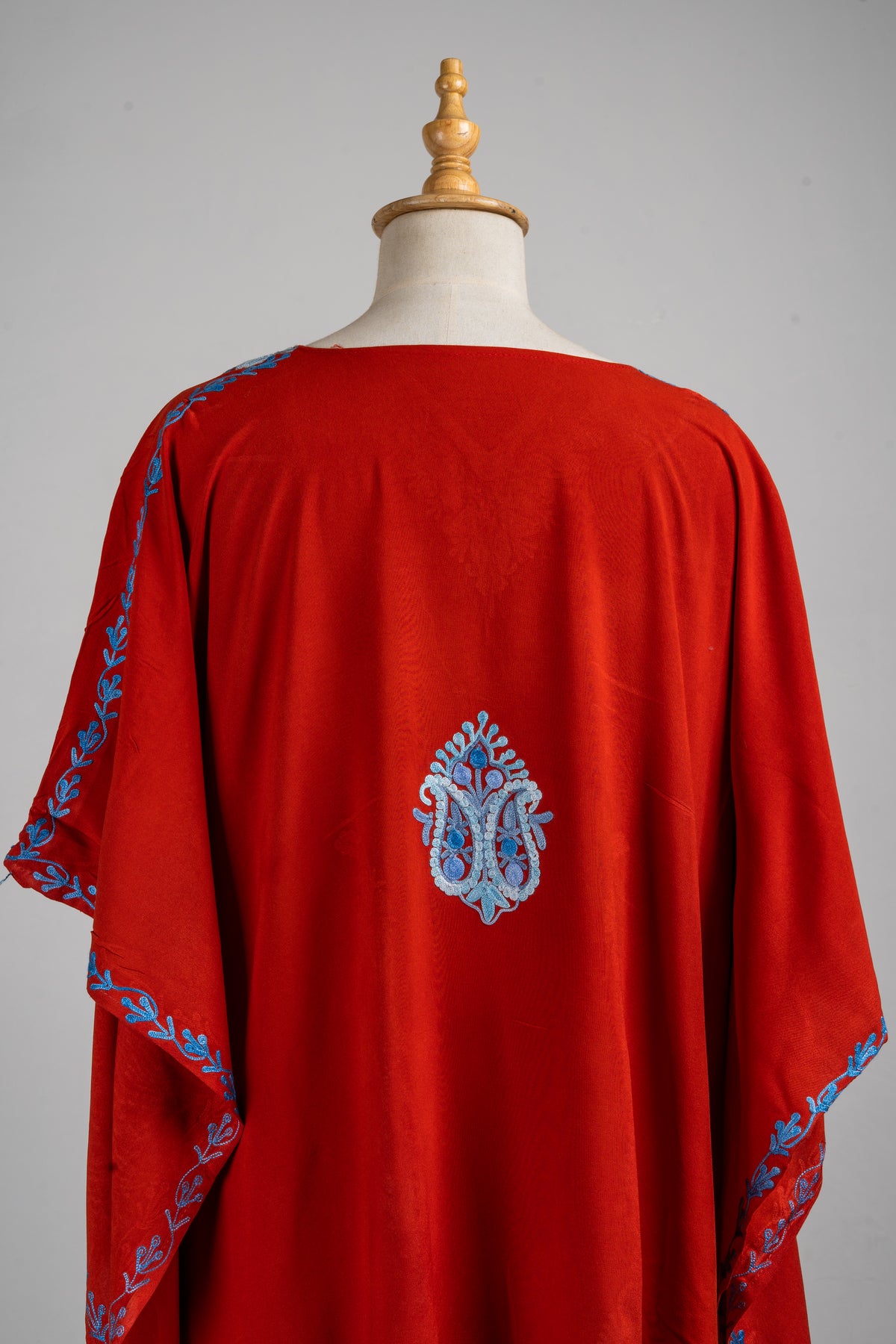 Upper back of the red kaftan with a small blue paisley motif and blue floral edging along the loose sleeves.