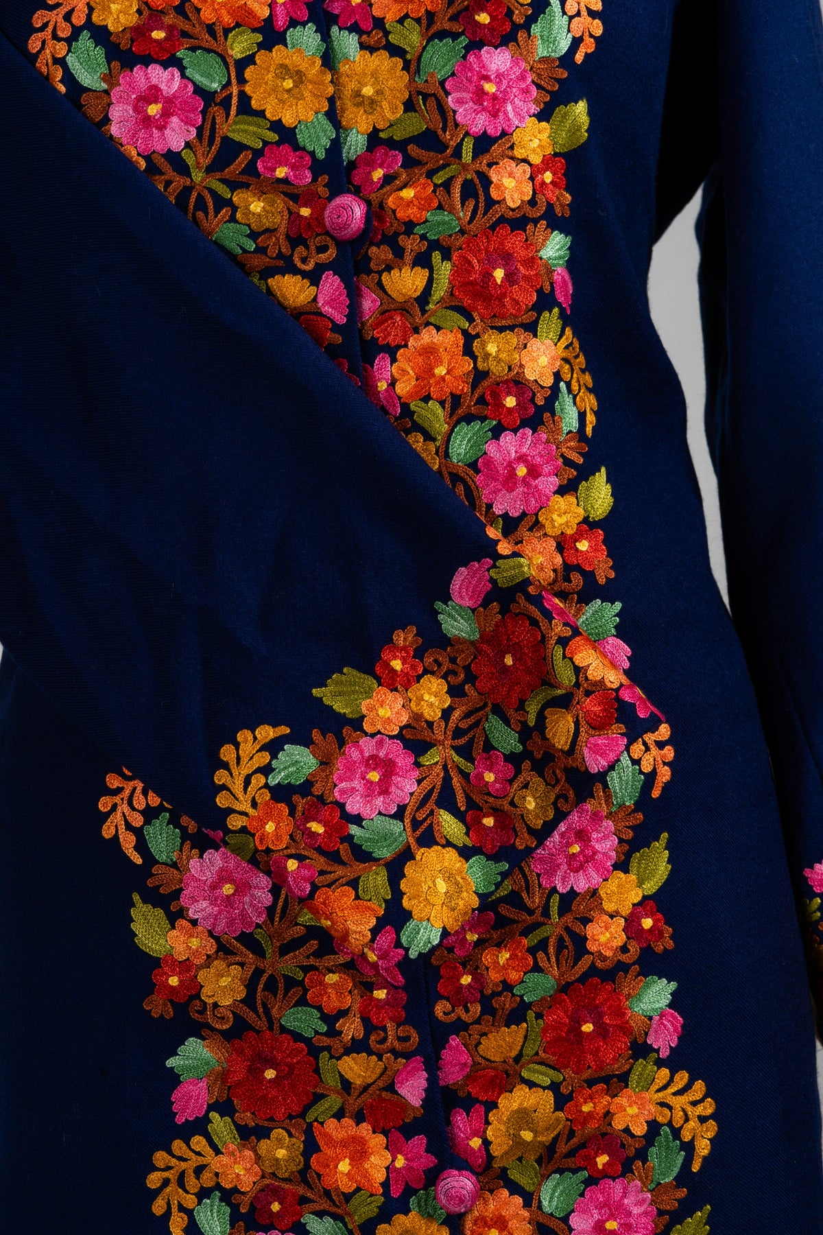 Detail of the navy jacket’s crossed sleeve and colourful floral cuff beside the densely embroidered front