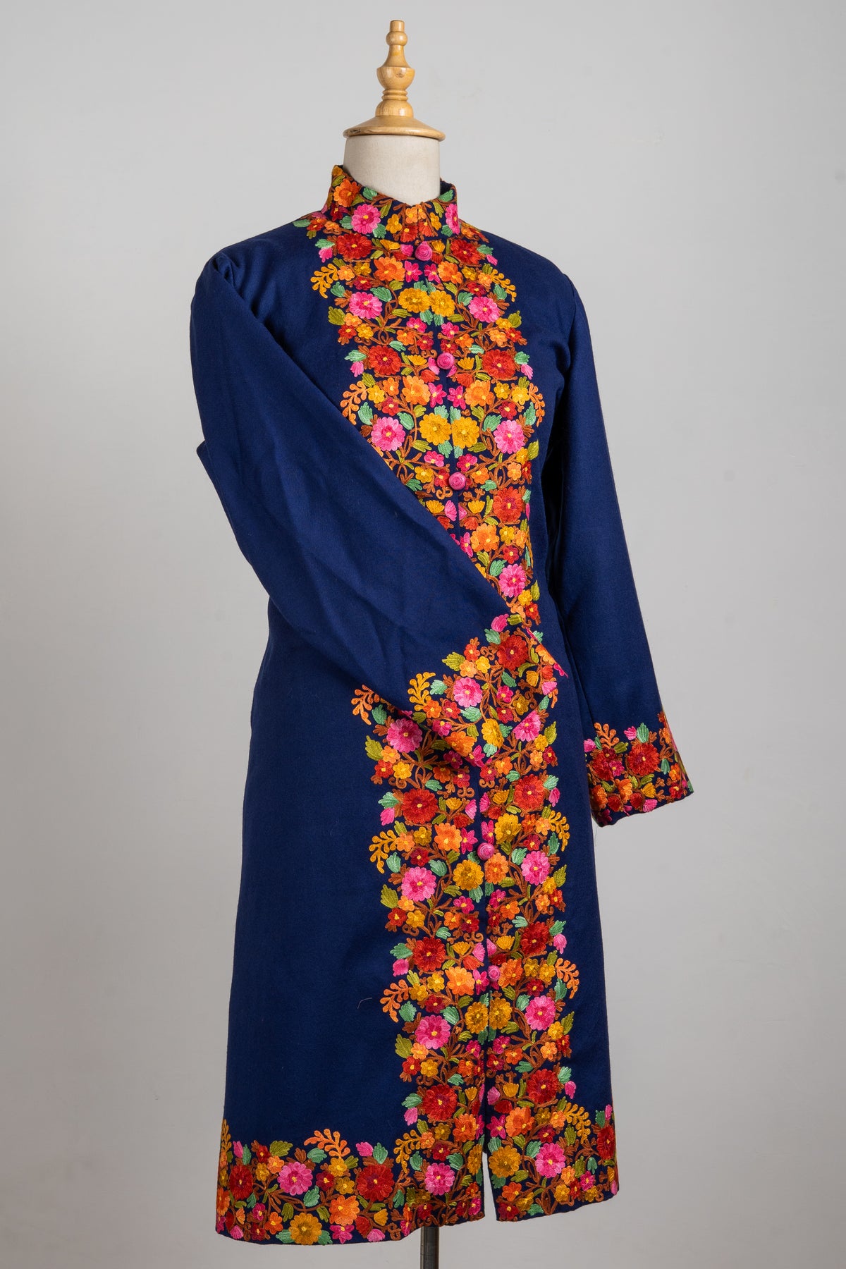 Angled full view of the navy long jacket, with bright floral embroidery down the front and around the cuffs and hem
