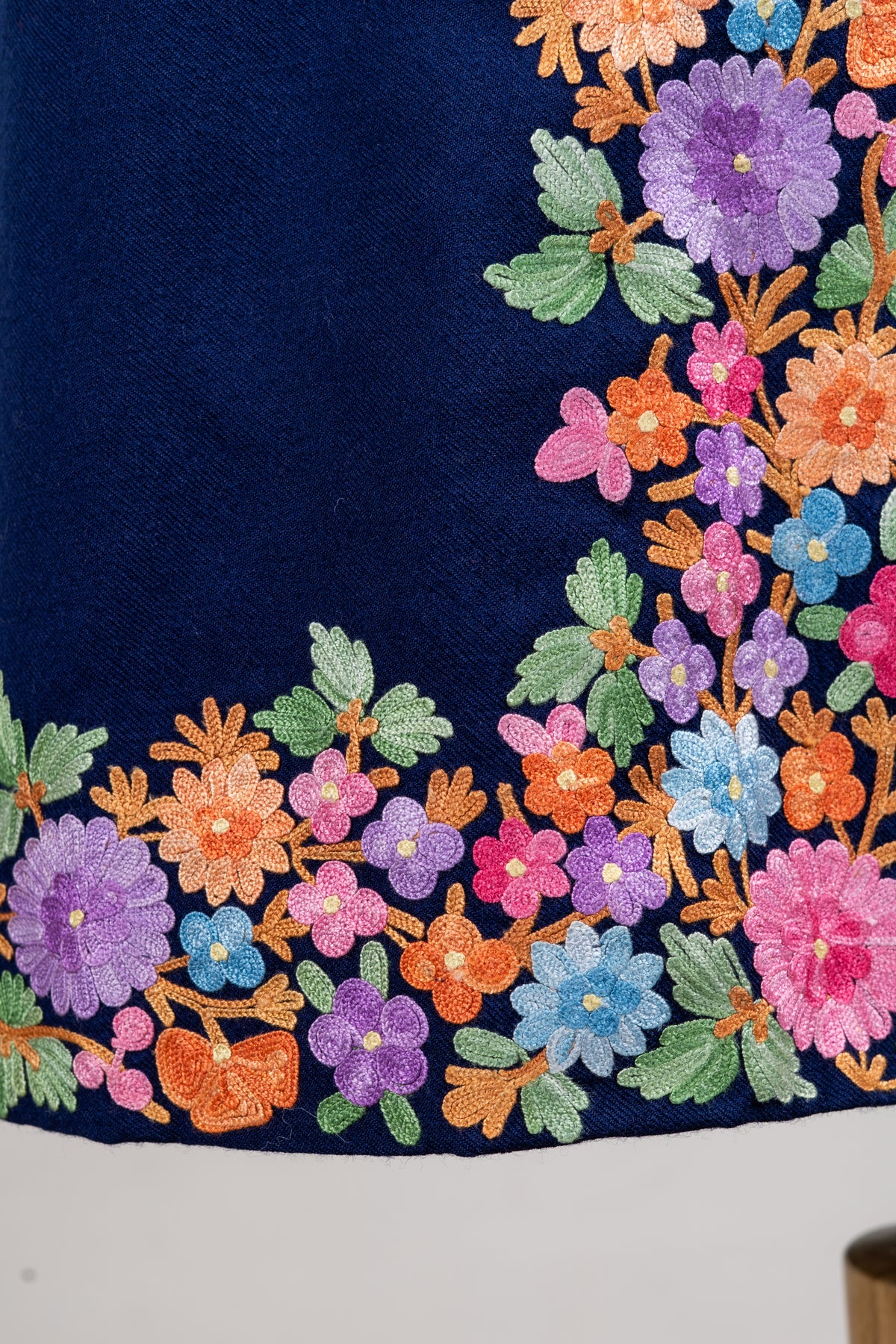 Close-up of a navy jacket's hem corner with pink, purple, blue and peach Aari flowers and pale green leaves