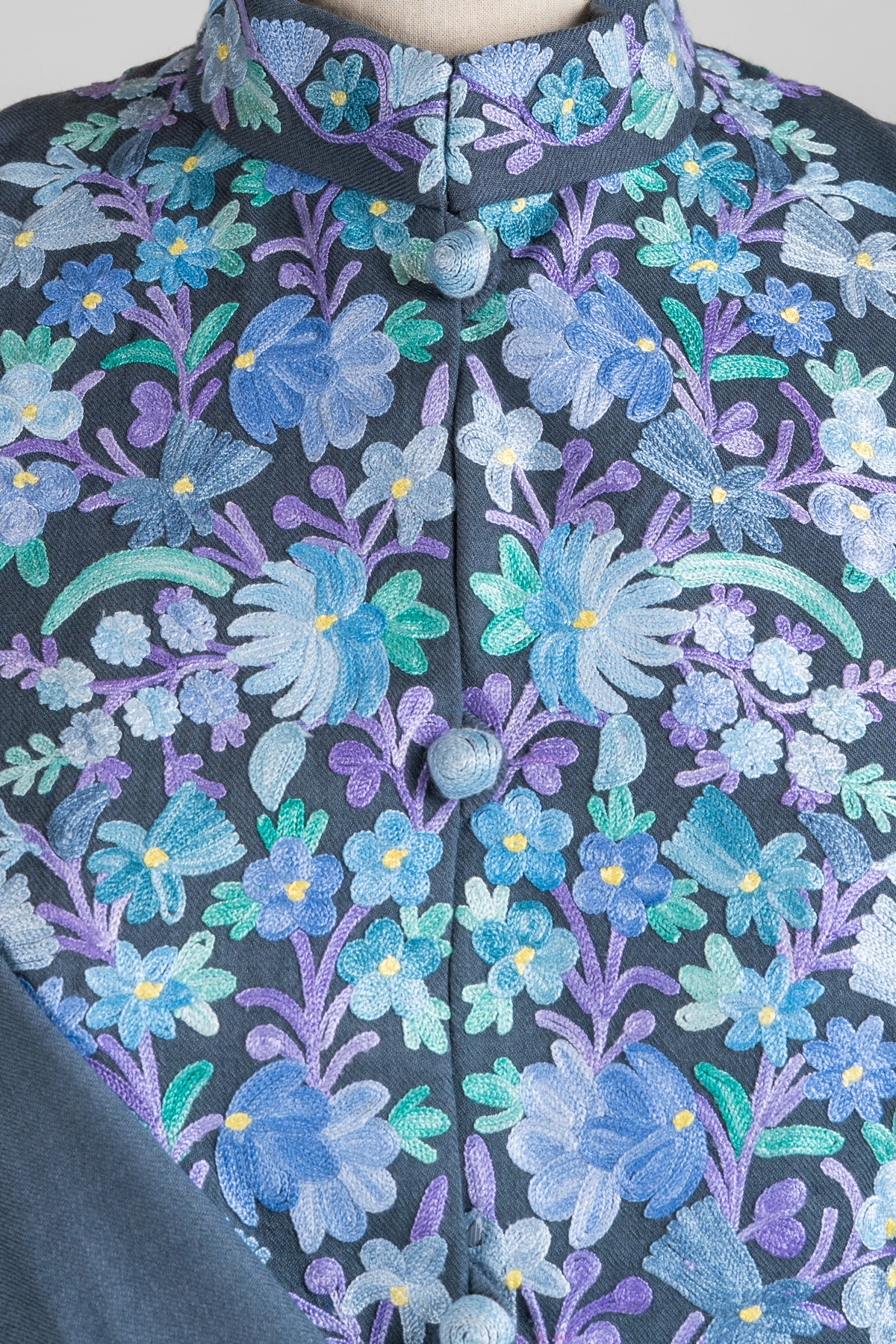 Close-up of the jacket collar and chest with blue flowers, lilac stems, teal leaves and pale blue covered buttons.