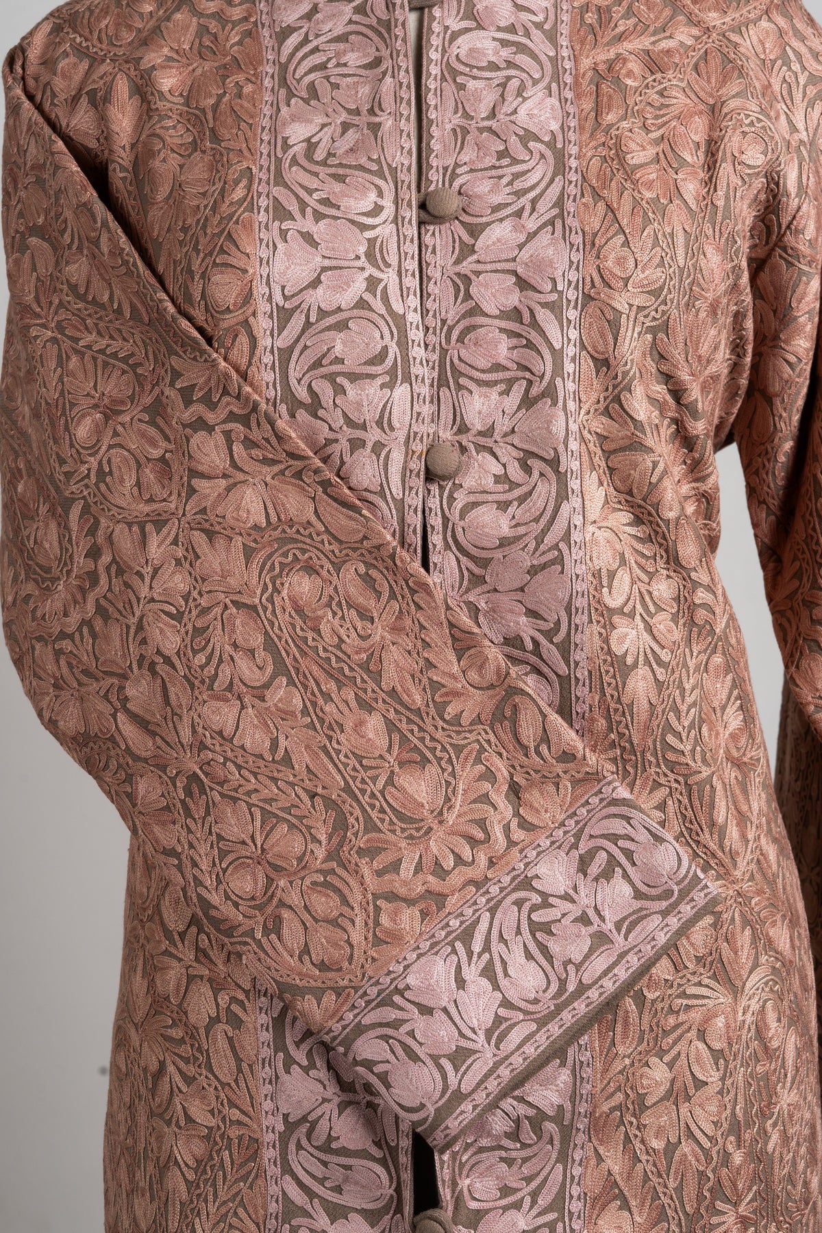 Detail of the dusty-rose jacket’s crossed cuff and front, showing dense floral embroidery and a broad pale patterned border