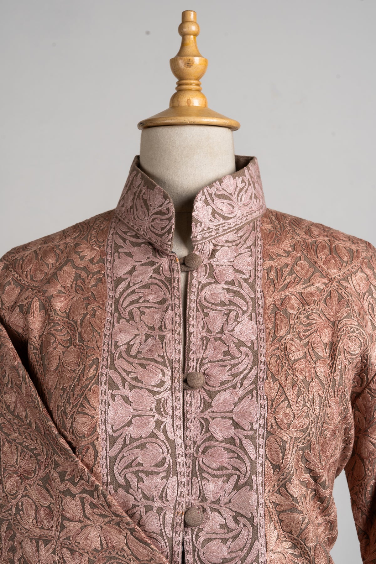 Close-up of the jacket’s stand collar and button placket, with pale blush floral bands and covered buttons