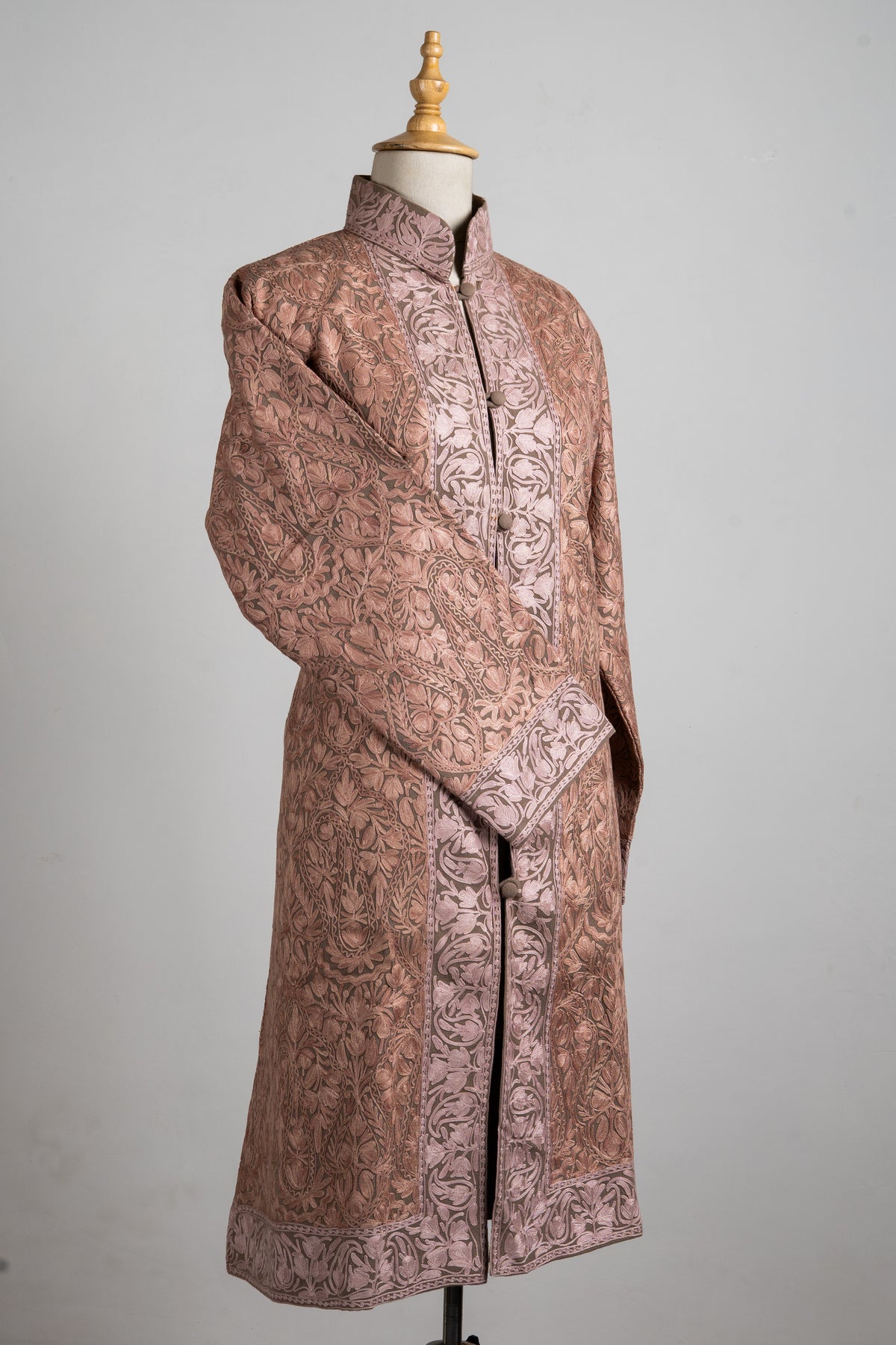 Angled full view of a dusty-rose Aari jacket, with floral vines, wide pale borders and one sleeve crossed