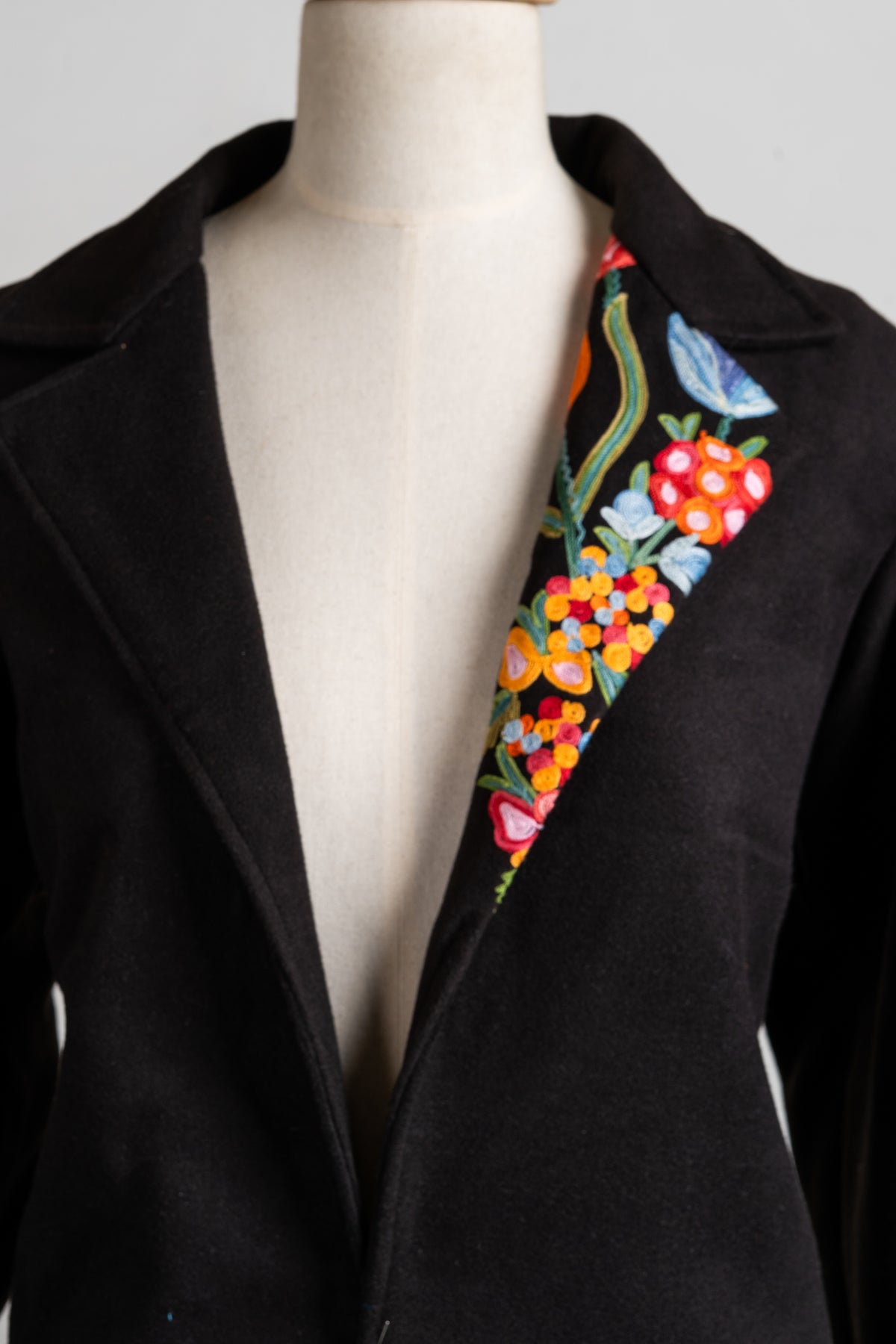 Closer view of the black blazer lapels, with a narrow strip of bright floral embroidery along one side.