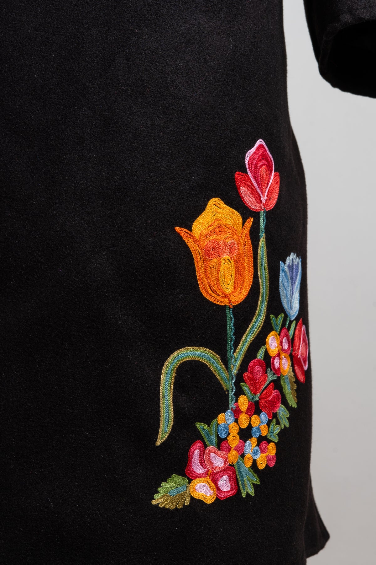 Lower front detail of the black blazer with orange, red and blue embroidered flowers on curling green stems.