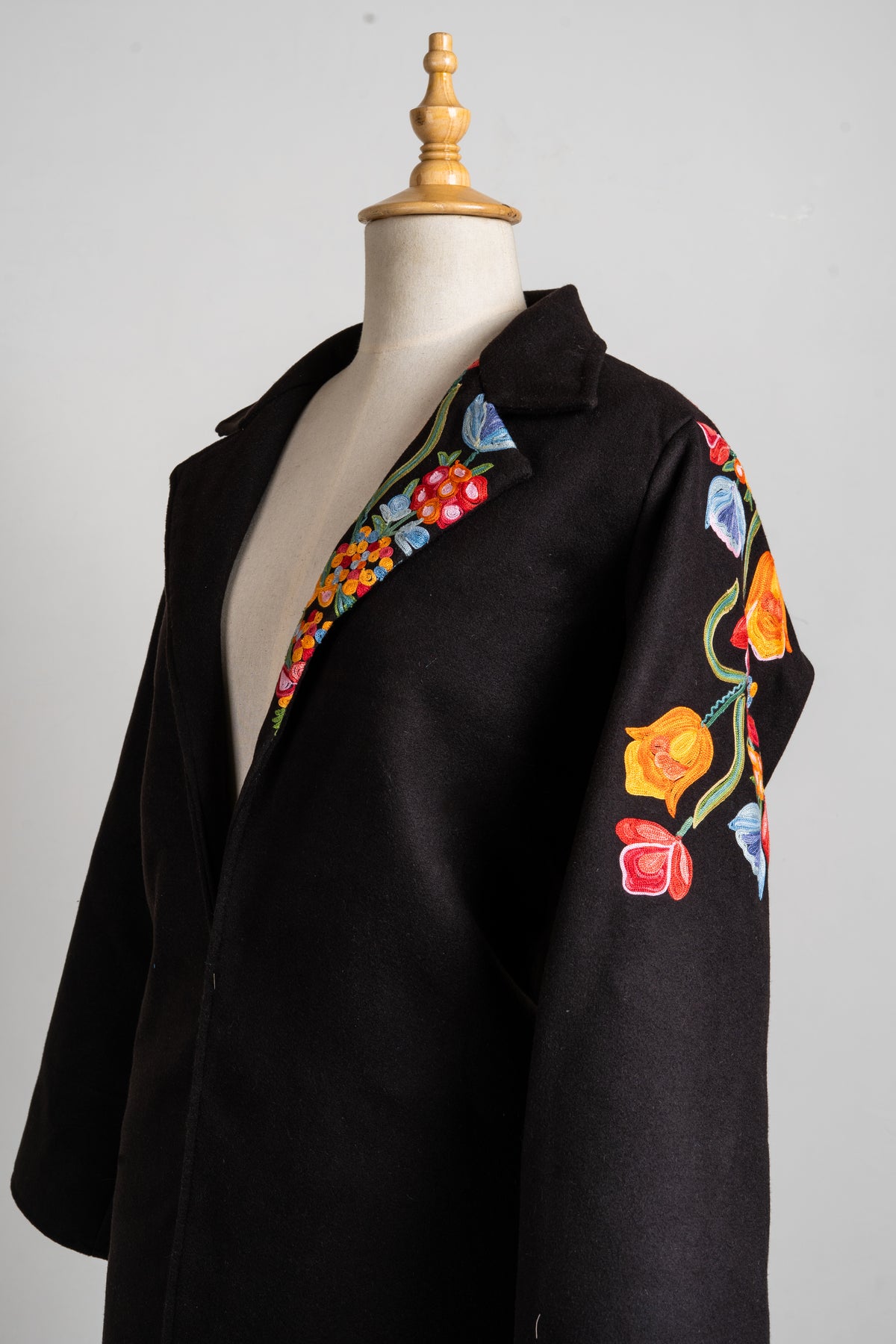 Angled upper-front view of the black blazer showing floral embroidery on one lapel and the outer sleeve.