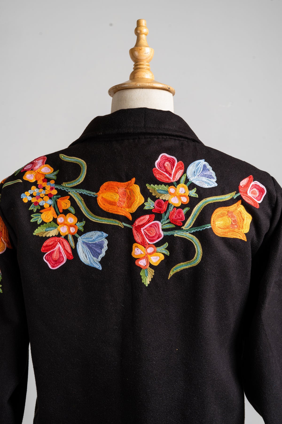 Upper back of the black blazer with a colourful floral spray stretching across the shoulders beneath the collar.