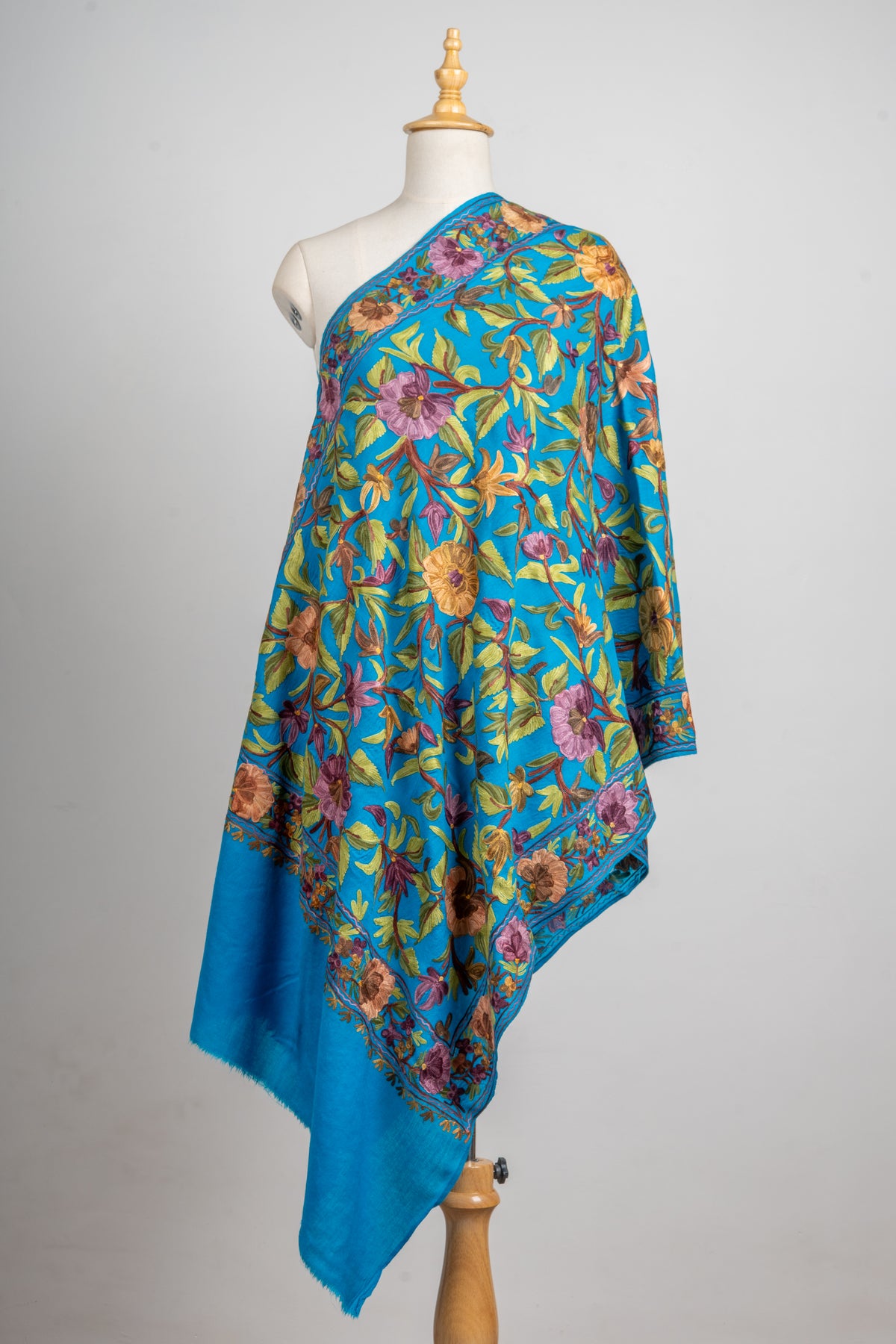 Front view of the peacock-blue stole on a mannequin, with large lavender and mustard flowers framed by a floral border