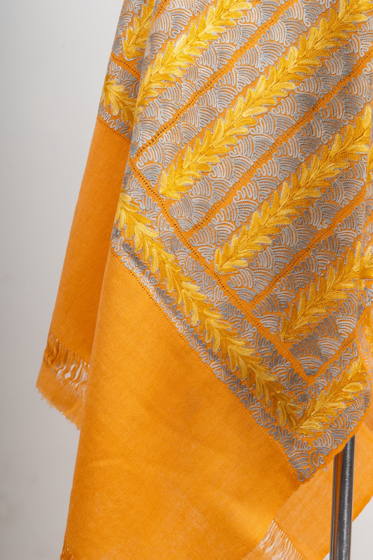 Detail of yellow Aari leaf trails and pale looped openwork on a golden stole, above a plain saffron-orange end