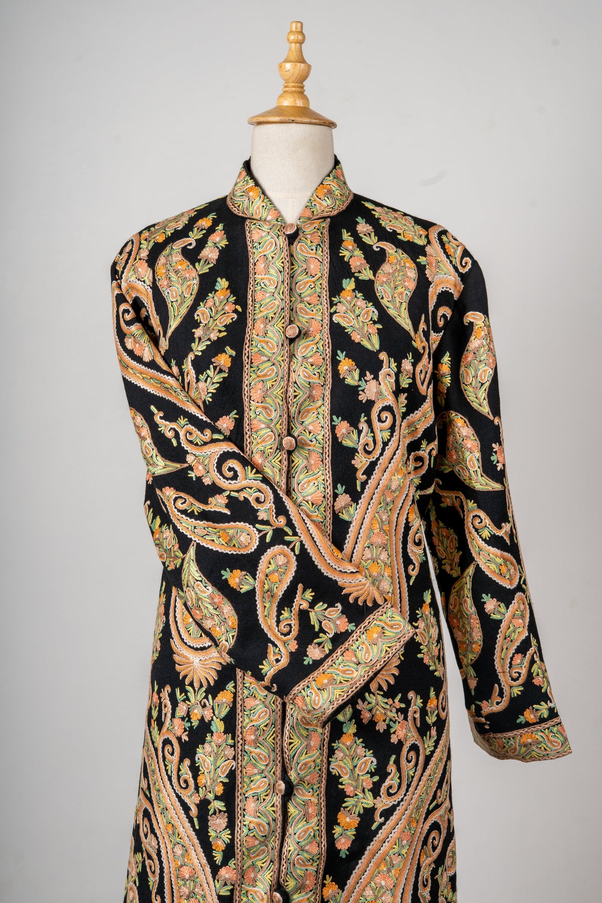 Upper front of a black jacket with peach-and-gold paisleys, an olive floral button band and an embroidered stand collar