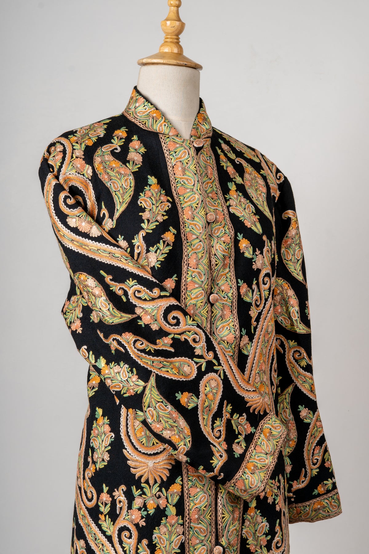 Close angled view of the black jacket’s crossed sleeve and chest, showing large paisleys filled with peach flowers and olive leaves