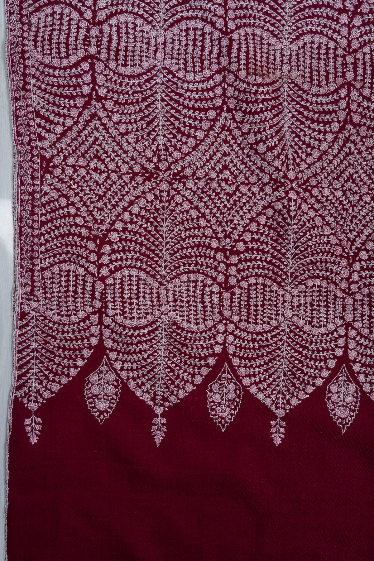 Close-up of the wine shawl's scalloped embroidered border, with small hanging floral motifs above the plain end