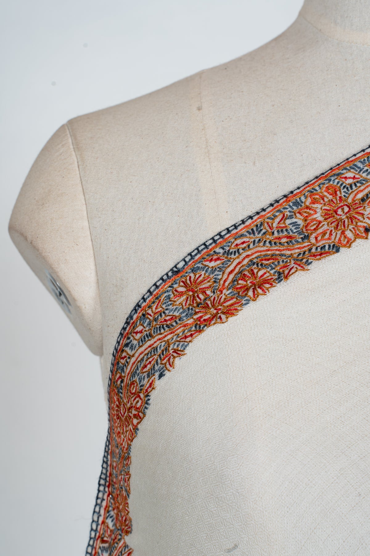 Shoulder close-up of the ivory shawl's orange flowers and blue-grey leafy Sozni embroidery