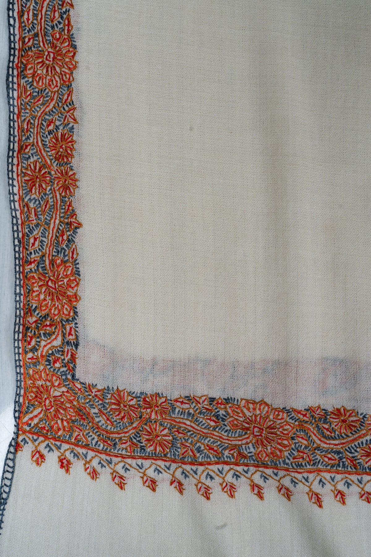 Corner detail of the ivory shawl with orange flowers, blue-grey foliage and fine stitched edging