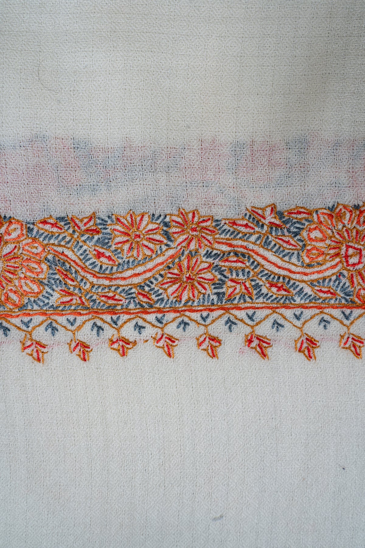 Close-up of the ivory shawl's orange floral border with blue-grey leaves and pendant-like motifs