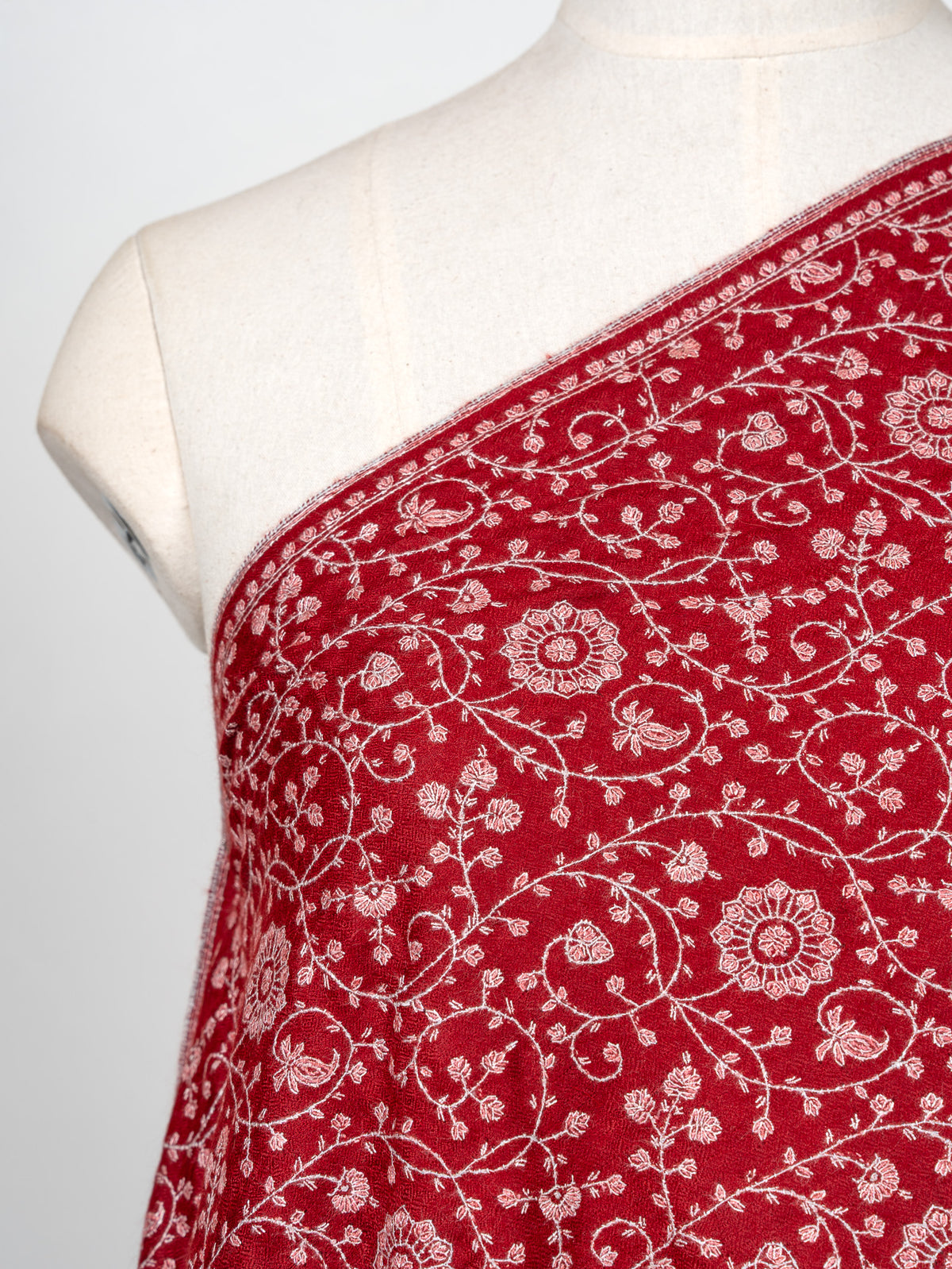 Close-up of ivory Sozni flowers and fine curling vines across the shoulder of a crimson Pashmina shawl