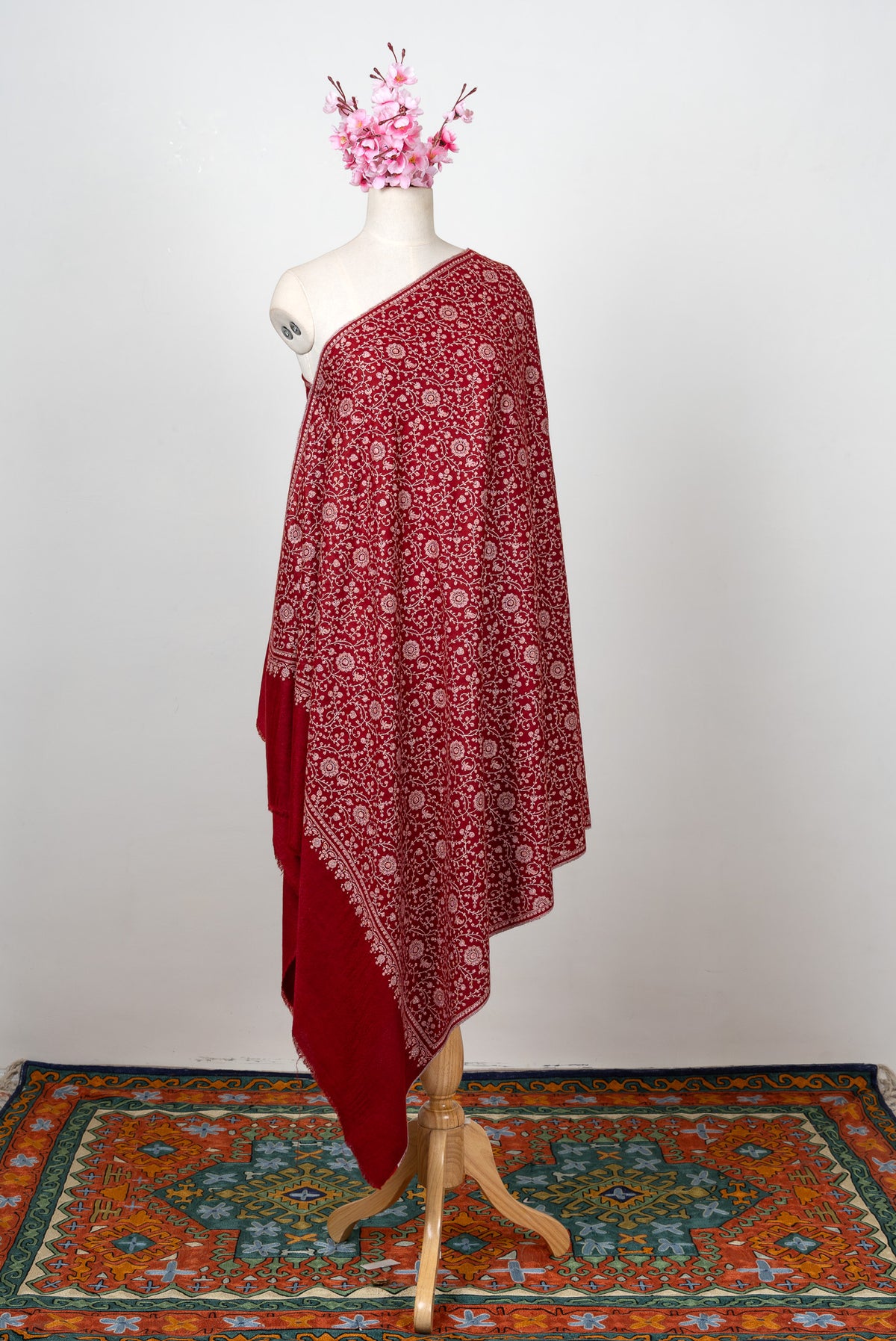 Full view of a crimson Pashmina shawl on a mannequin with all-over ivory Sozni flowers and vines