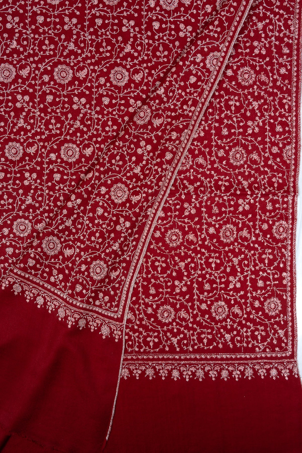 Overlapping crimson shawl corners showing ivory Sozni floral vines and matching embroidered borders