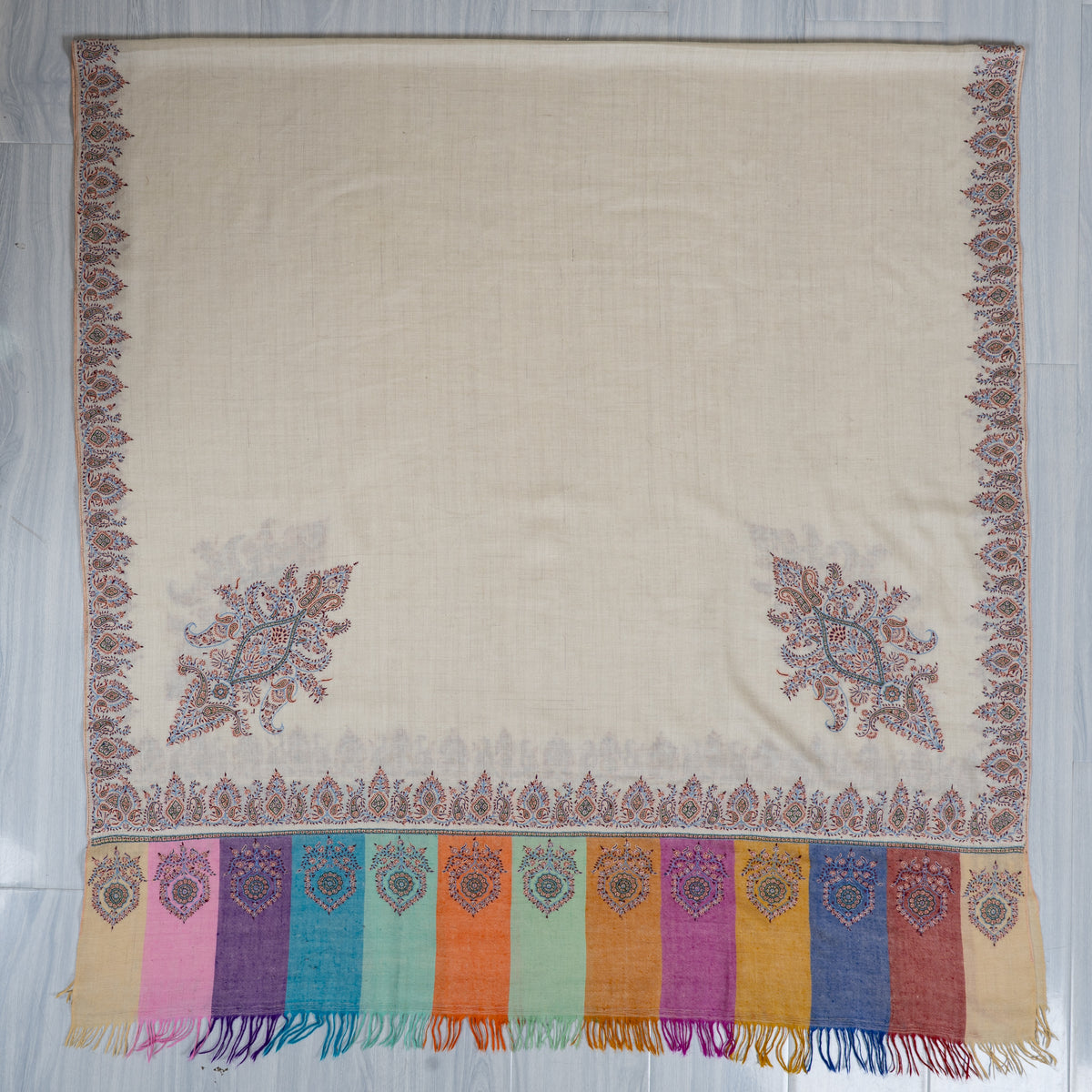 Ivory shawl spread flat, with two large corner motifs, narrow decorative borders and a multicoloured fringed end