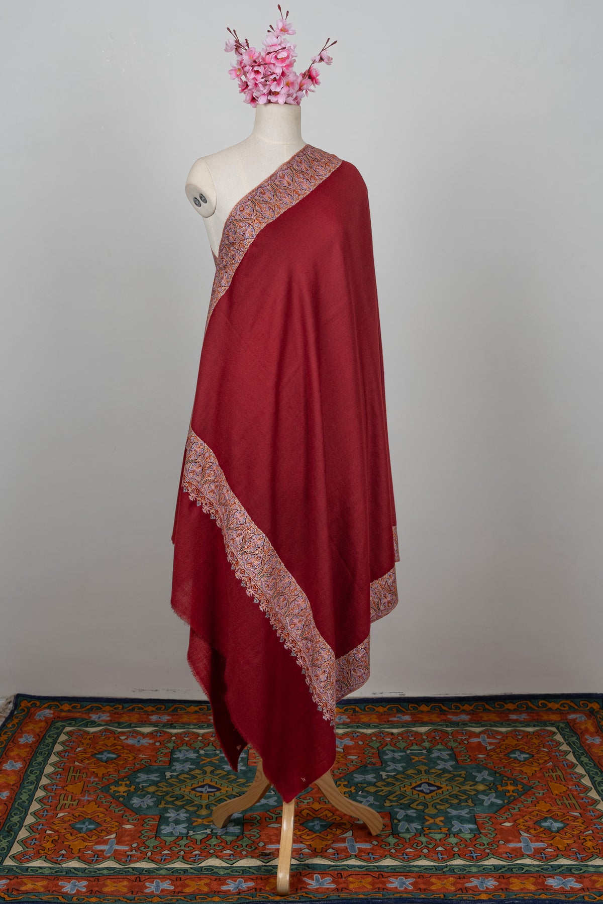 Full-length crimson Pashmina shawl on a mannequin with pale Sozni borders around a plain field