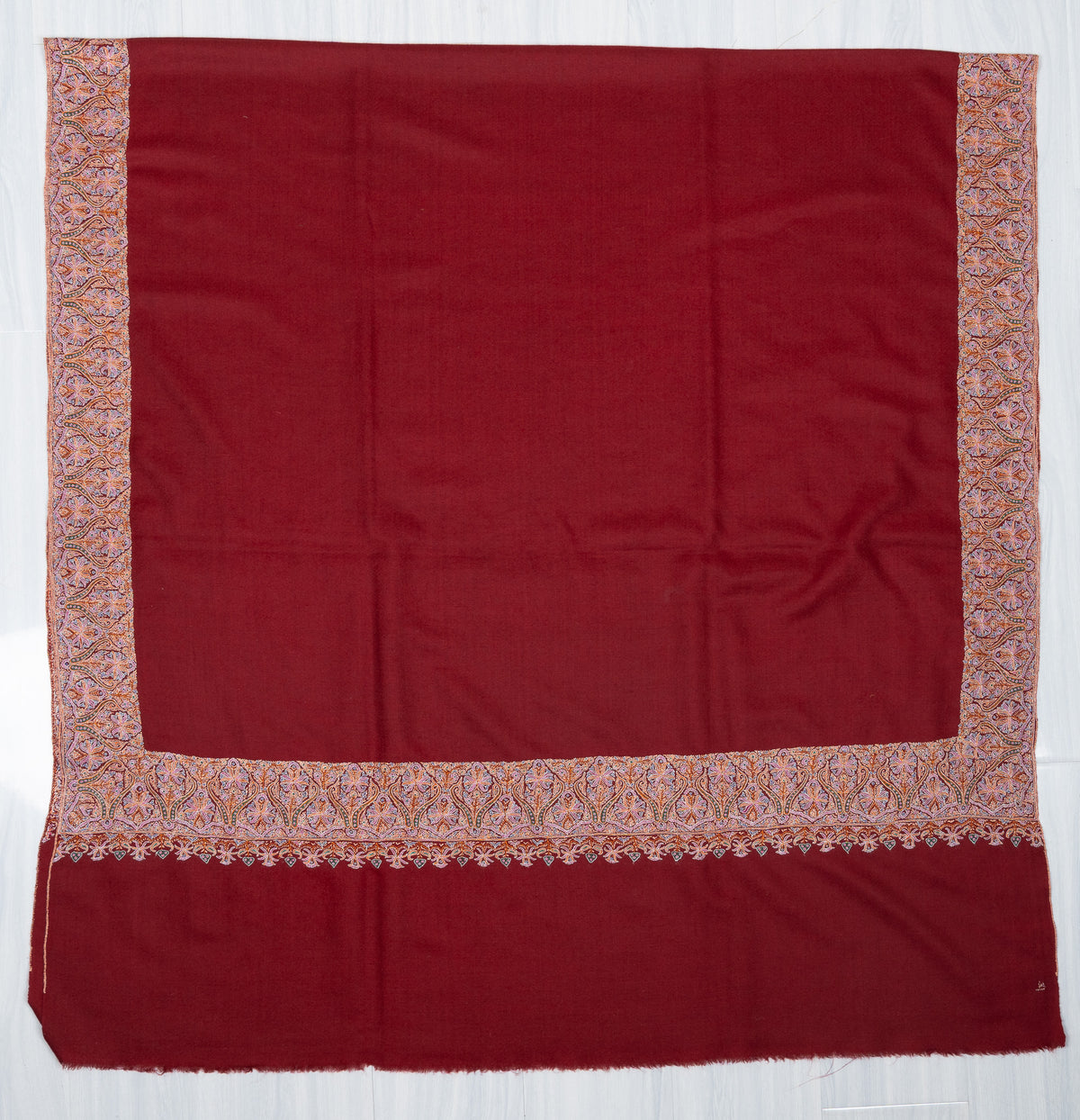 Crimson Pashmina shawl laid flat with pale multicoloured borders framing a plain centre and end panel