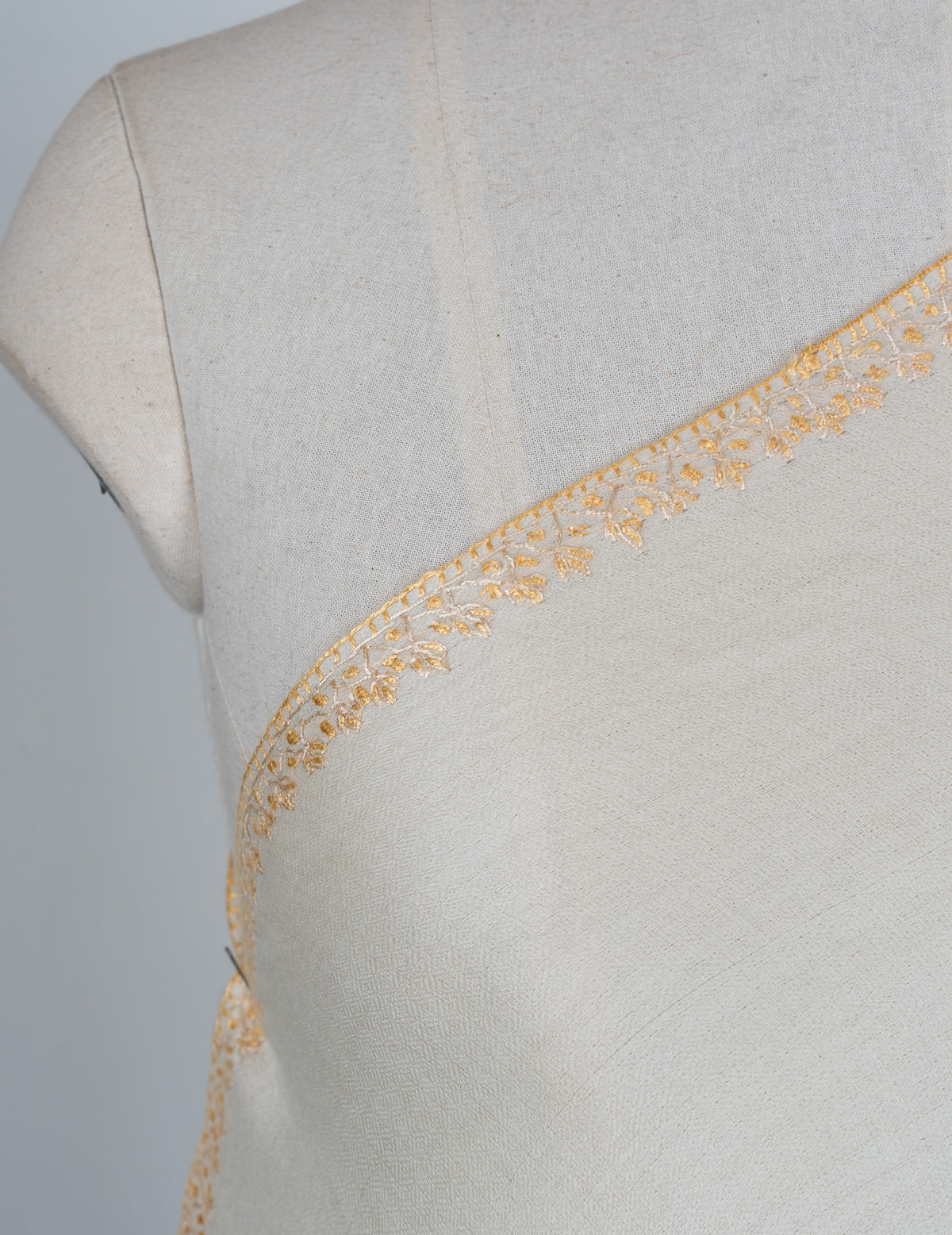 Shoulder detail of an ivory shawl showing delicate pale golden Sozni leaves along the narrow edge